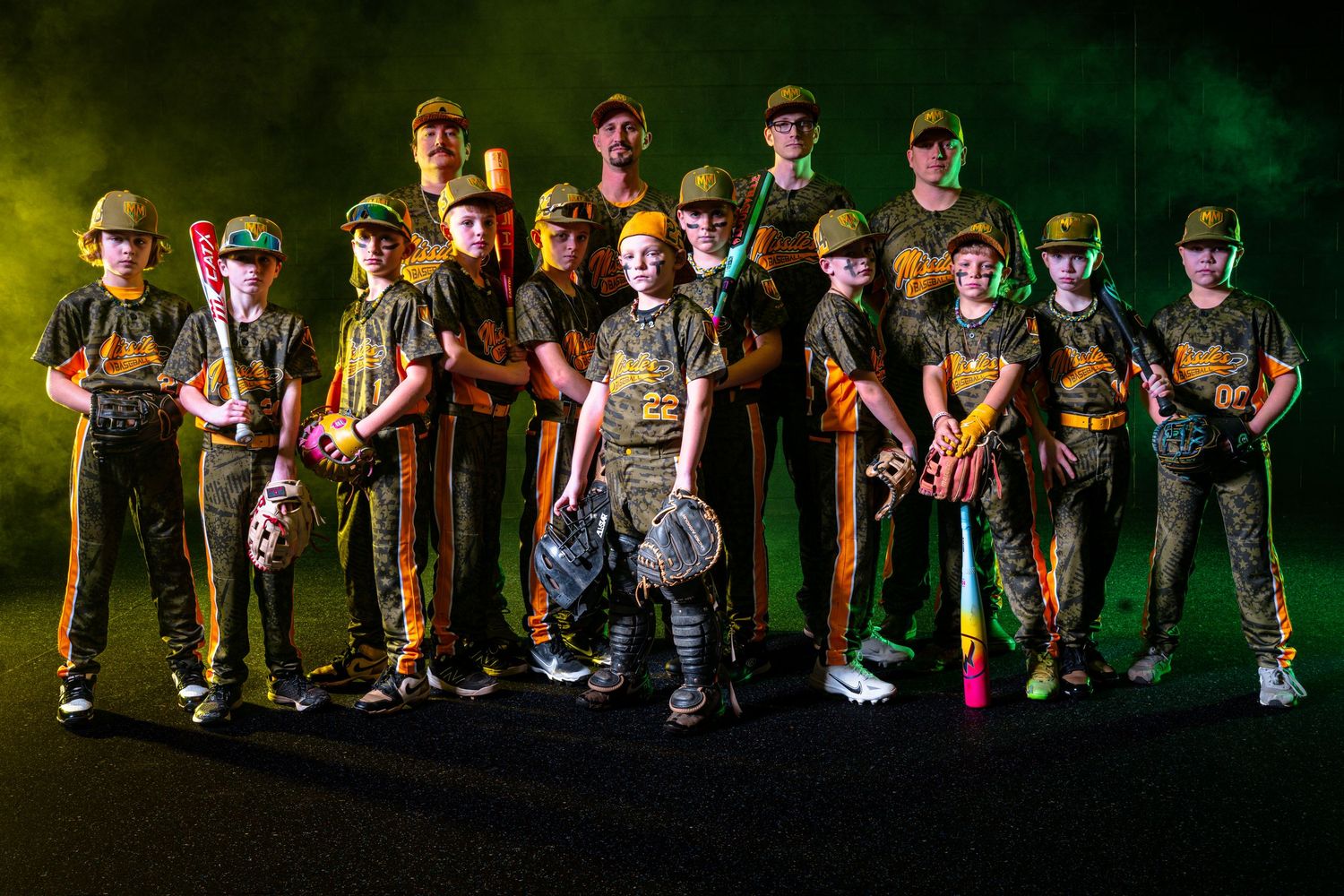 Youth baseball team in camouflage uniforms posing with bats and gear against a dramatic dark green backdrop.