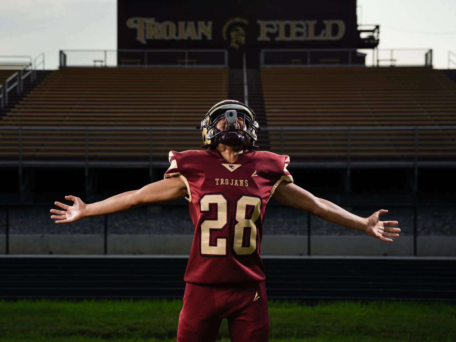 Football player #28 in Trojans uniform poses with arms spread wide on Trojan Field stadium turf.