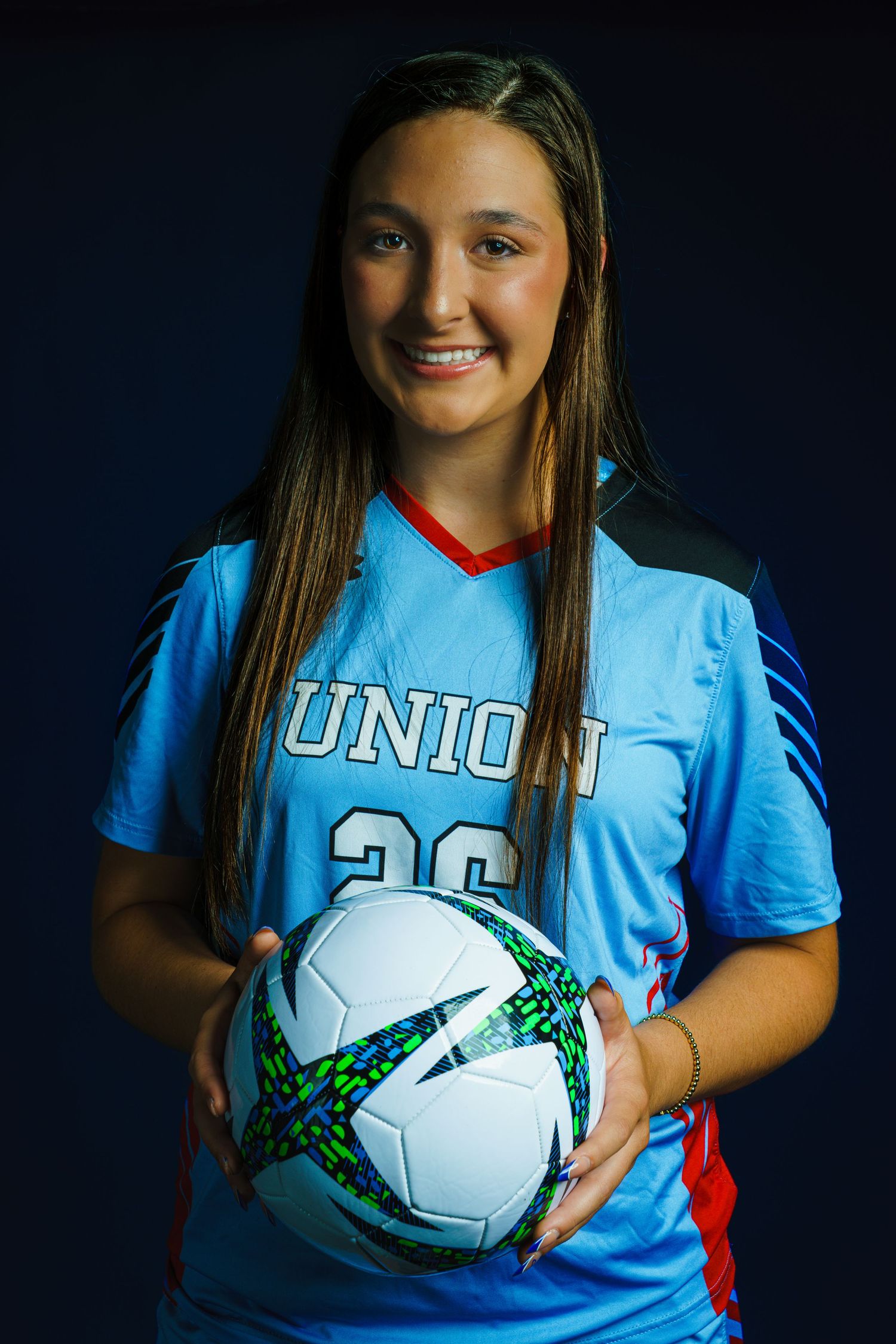 Young female soccer player in blue Union jersey holding a soccer ball, posing for a team portrait photo.