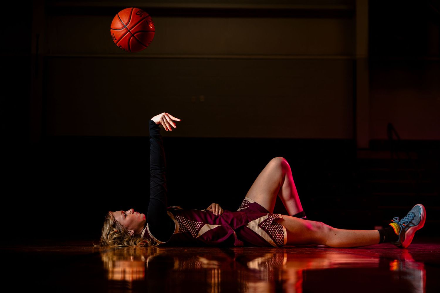 Basketball players leap and compete for a rebound during an intense indoor game under dramatic lighting.
