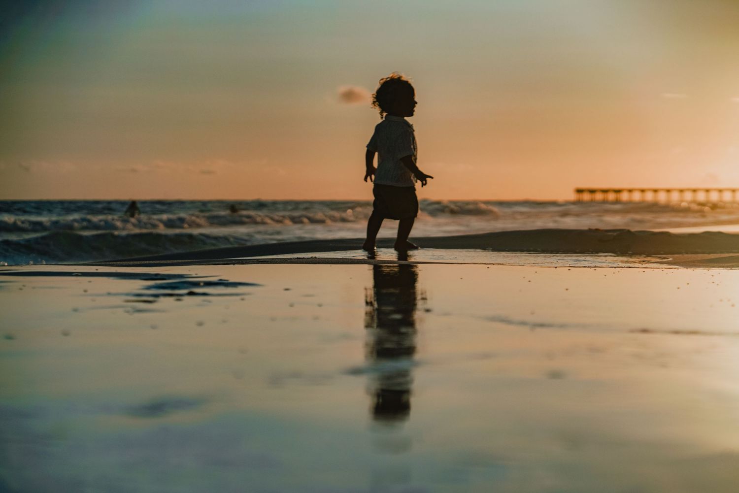 Silhouette of person walking on reflective beach at sunset.