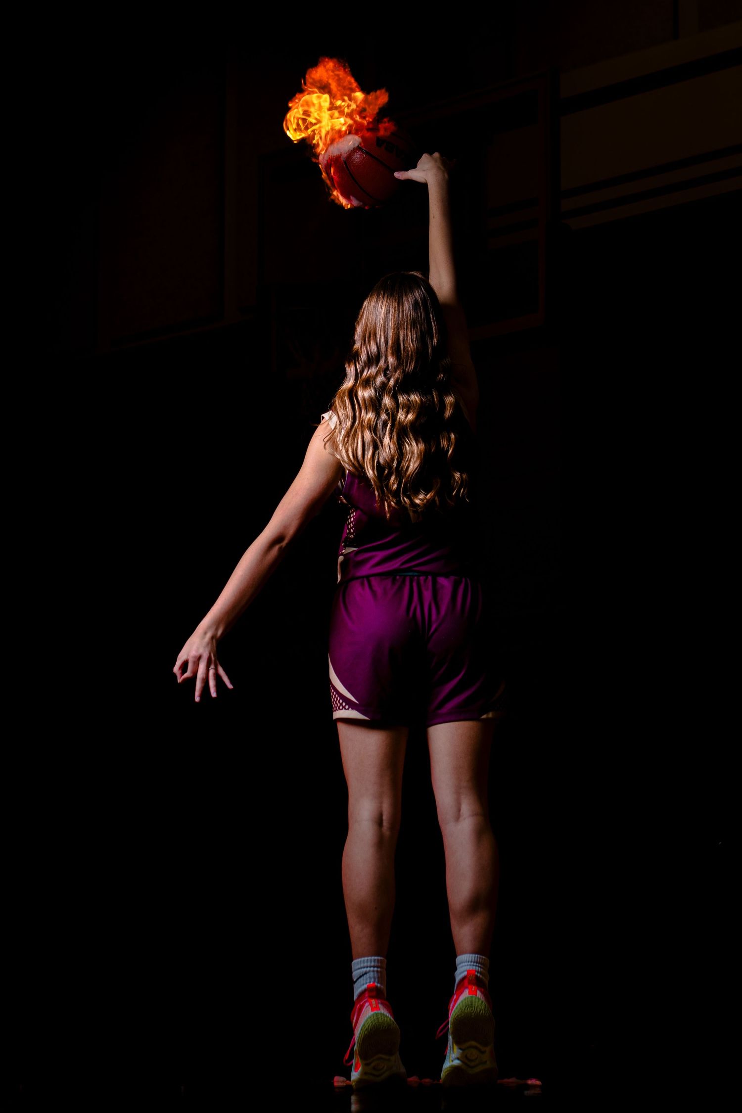 Woman in purple shorts holding a flaming basketball aloft in a dramatic dark studio setting.