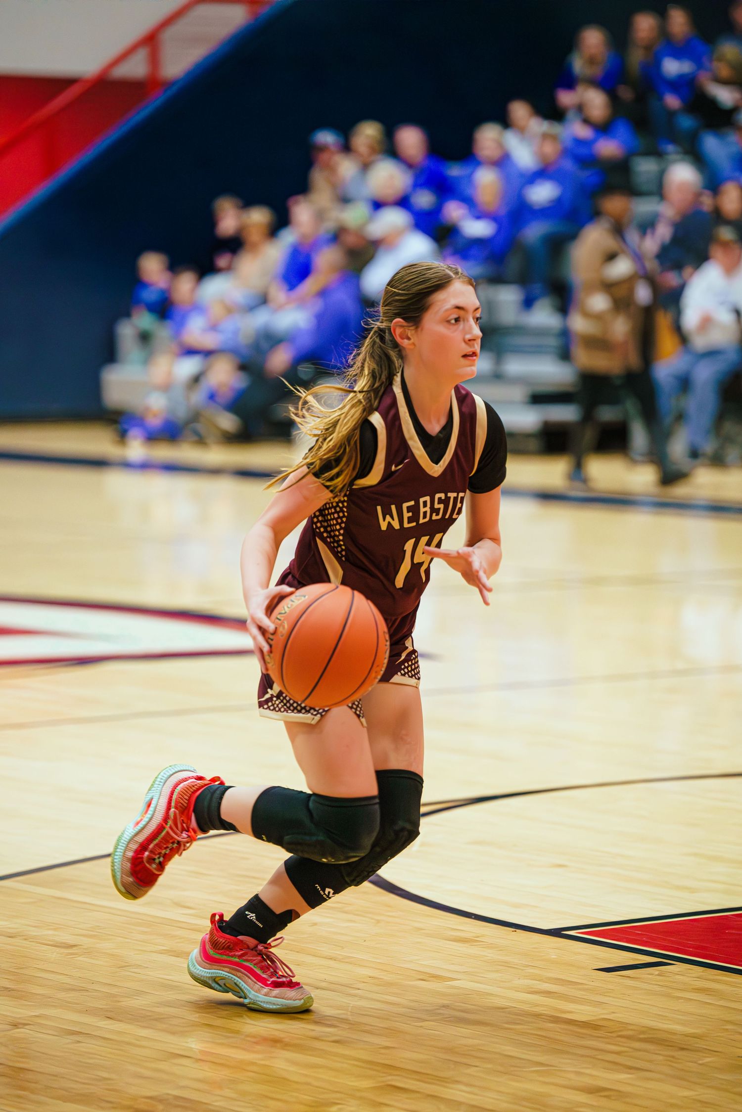 Webster girls basketball player dribbles down court in maroon uniform during competitive high school game.