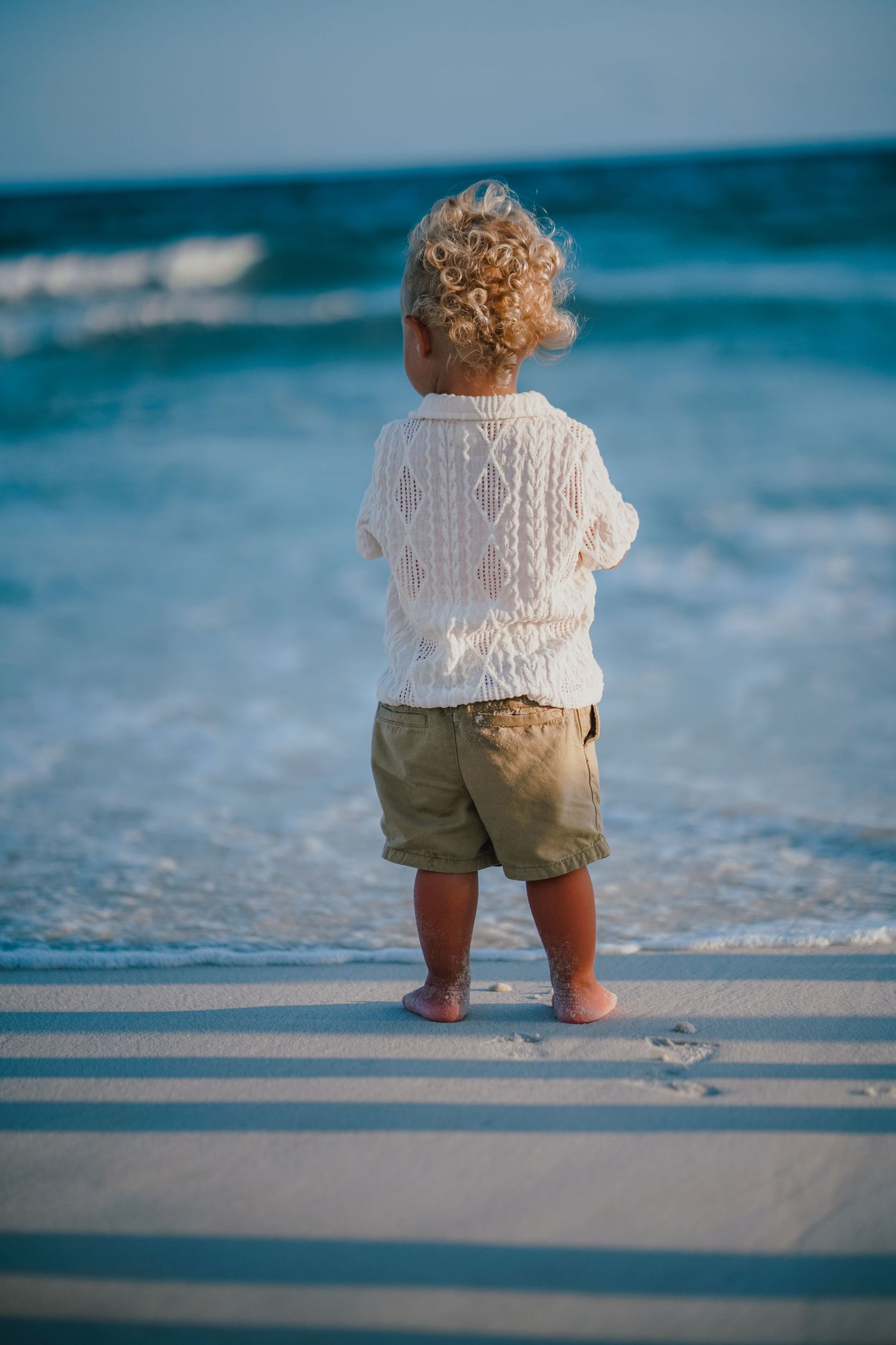 Small child standing at ocean's edge wearing white top and khaki shorts.