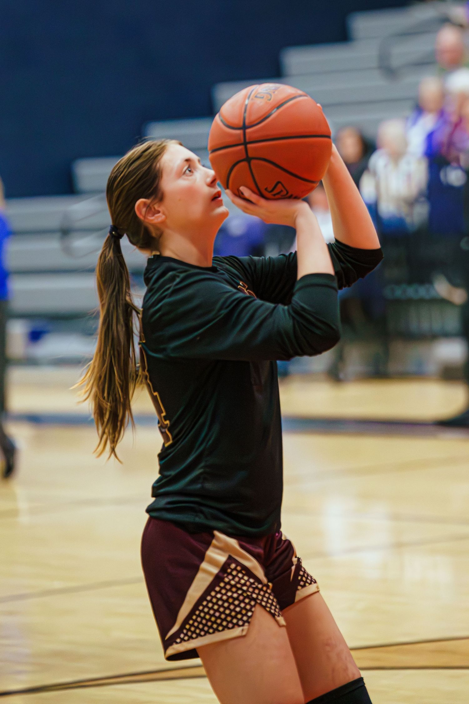 Young female basketball player in dark uniform shooting a basketball during an indoor game.