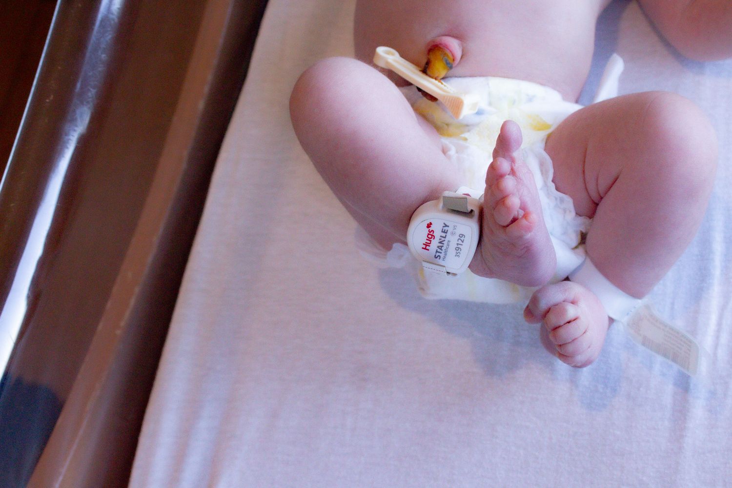 Newborn baby in diaper lying in hospital bassinet with identification tag attached.