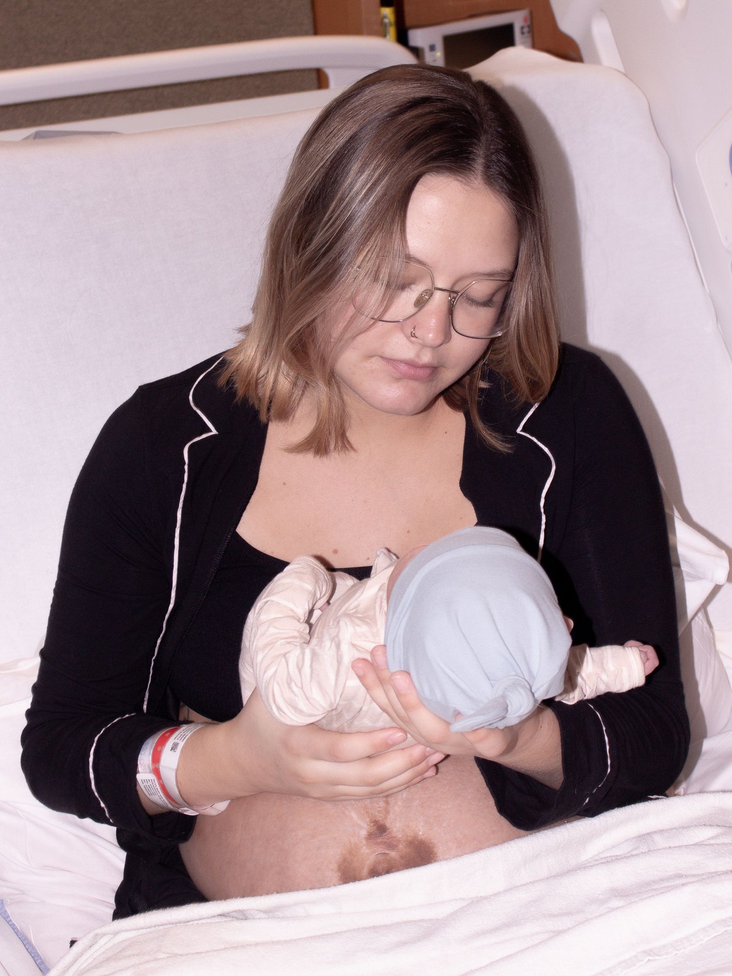 New mother in hospital bed breastfeeding her newborn baby wrapped in blue.