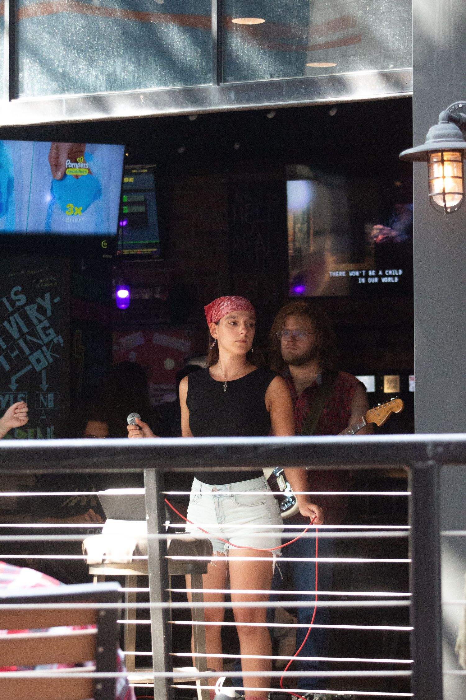Female singer with red bandana and guitarist performing at outdoor bar venue.