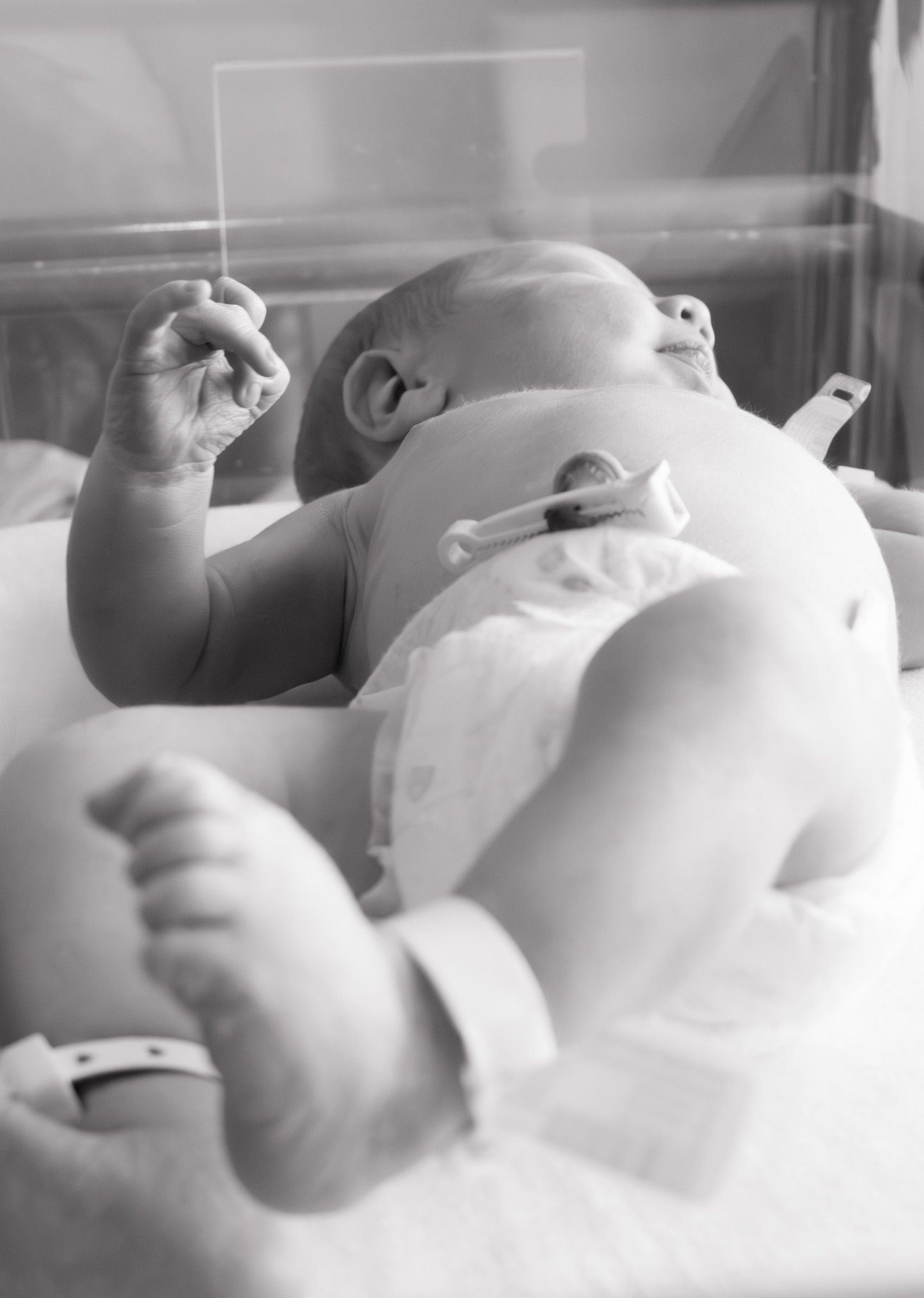 Black and white photo of newborn baby in hospital bassinet with ID wristband and diaper.
