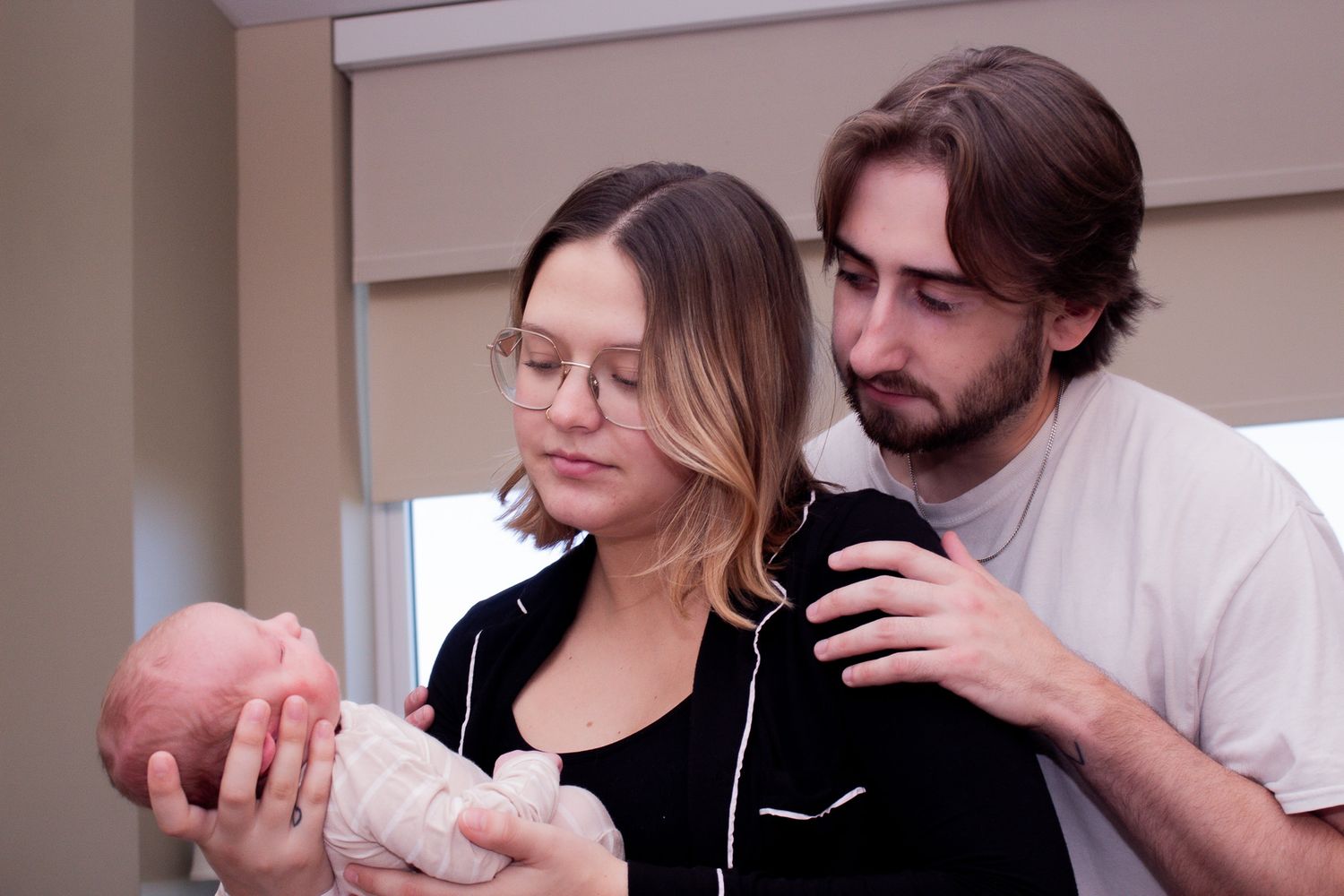 New parents in hospital room tenderly holding and gazing at their newborn baby.