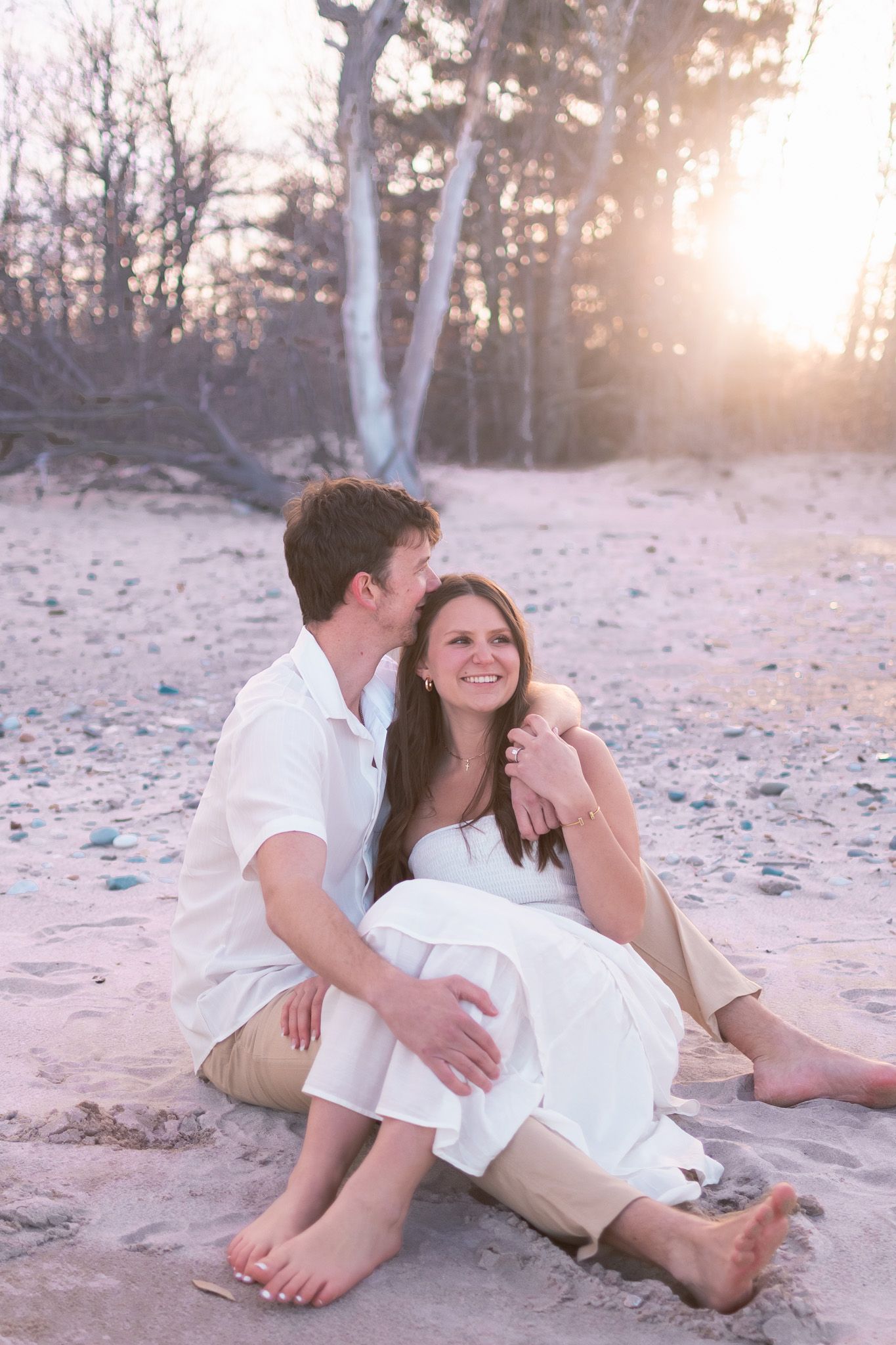 A happy couple sitting together on a sandy beach at sunset, embracing in warm golden light.