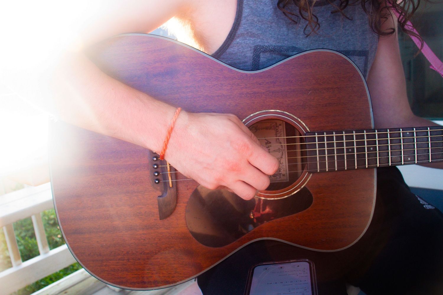 Close-up of hands strumming a mahogany acoustic guitar on a sunny porch.