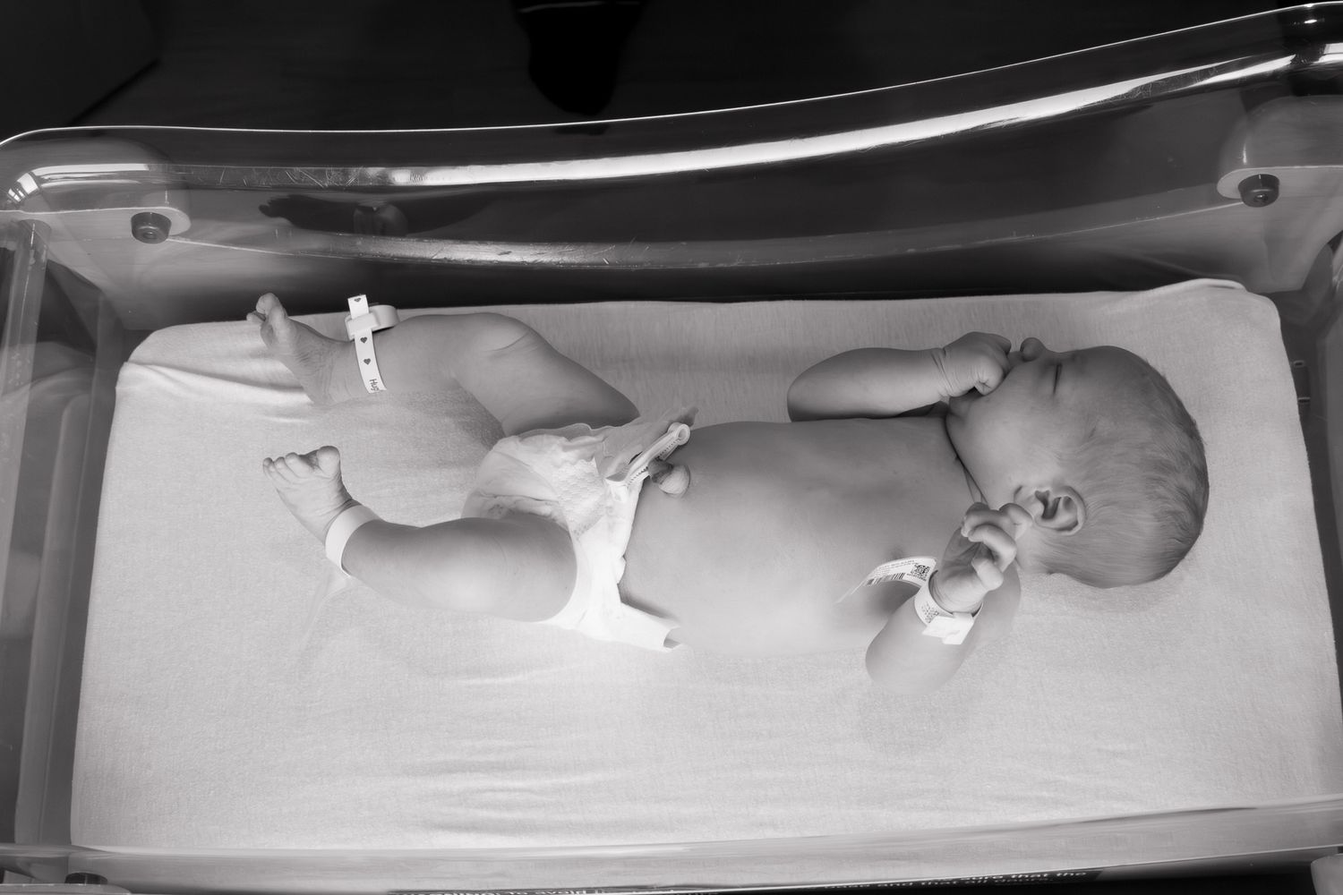Black and white photo of newborn baby lying in hospital bassinet wearing diaper.