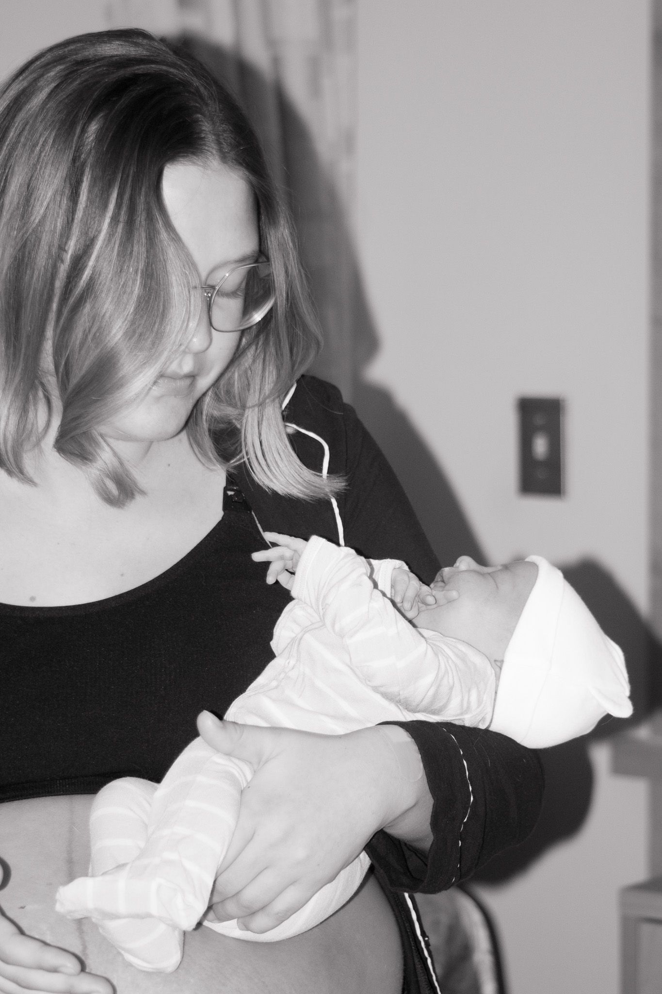 Black and white photo of a woman in black top cradling a newborn baby.
