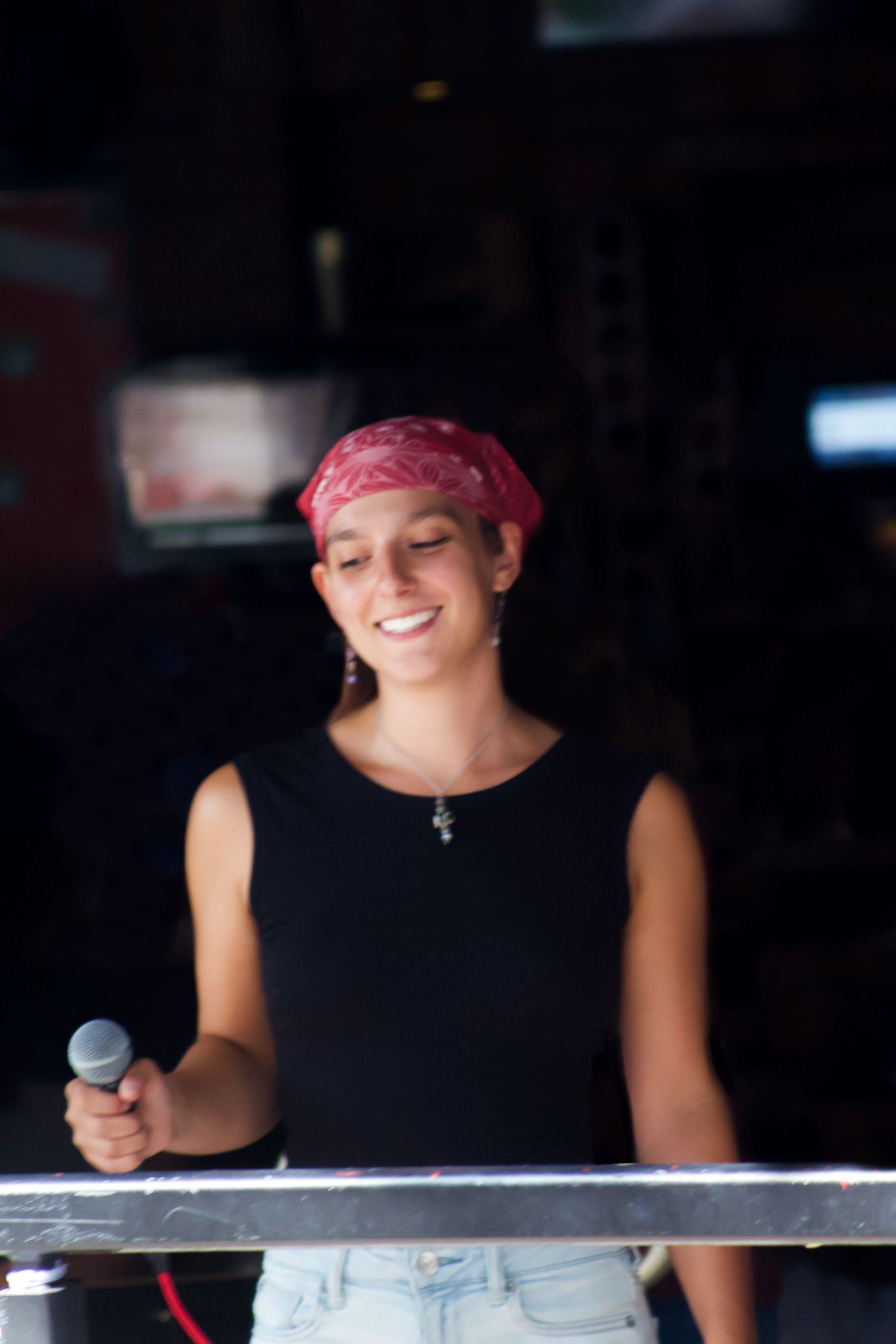 Smiling female performer holding microphone wearing red bandana at live music event.