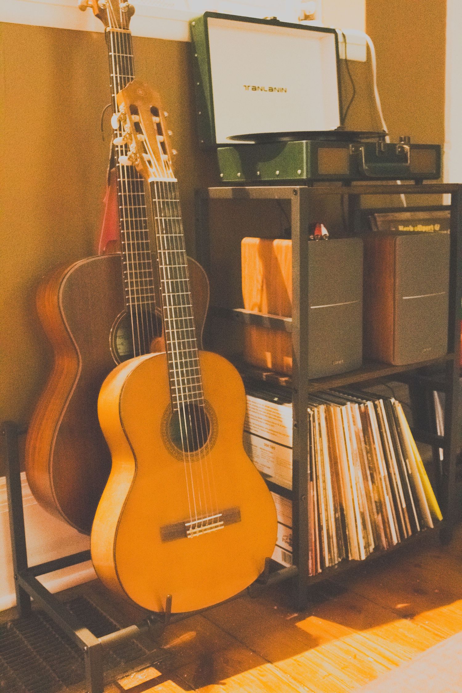 Two acoustic guitars leaning against a shelf with vinyl records and audio equipment.