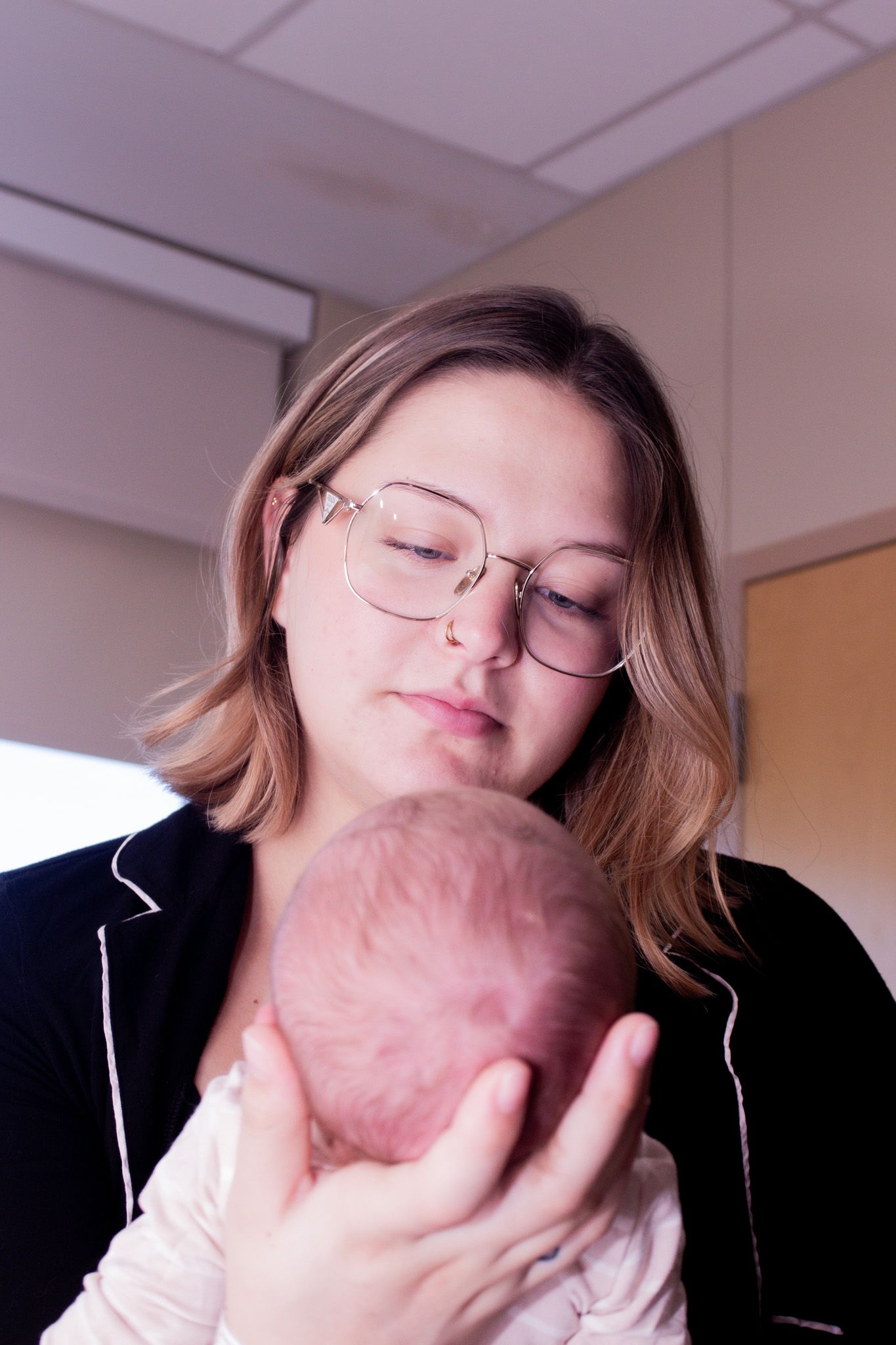 New mother in black top gently cradling her newborn baby while looking down lovingly.