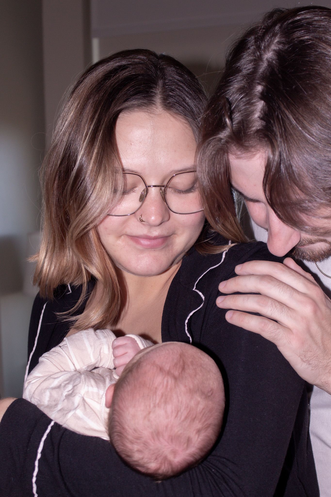 New parents lovingly gazing down at their newborn baby wrapped in white cloth indoors.