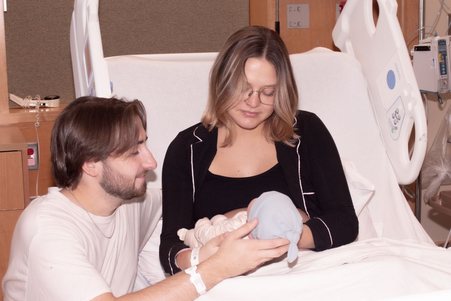 New parents in hospital room sharing a tender moment with their newborn baby.
