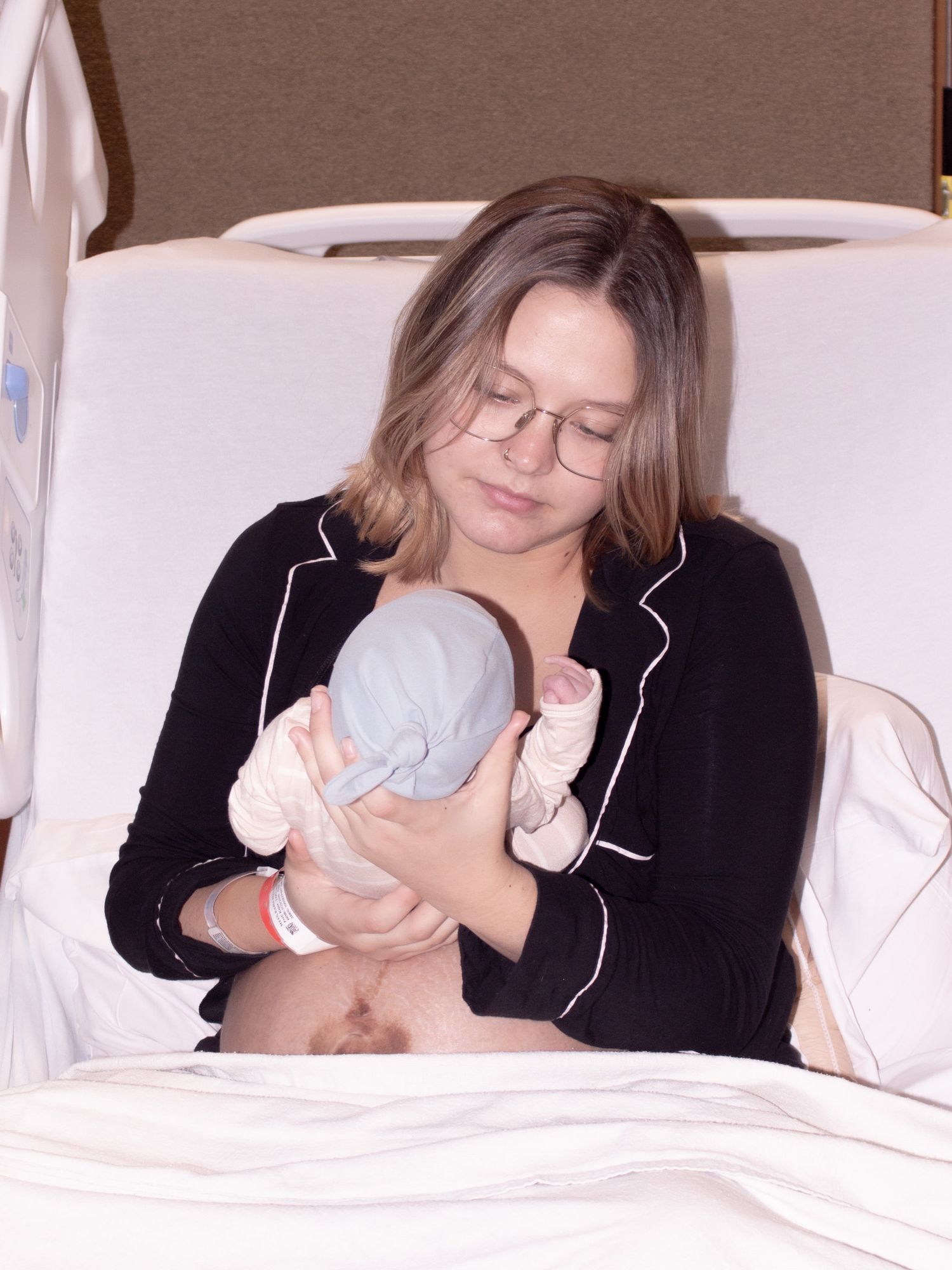 New mother sitting in hospital bed wearing glasses holding and bonding with her newborn baby.