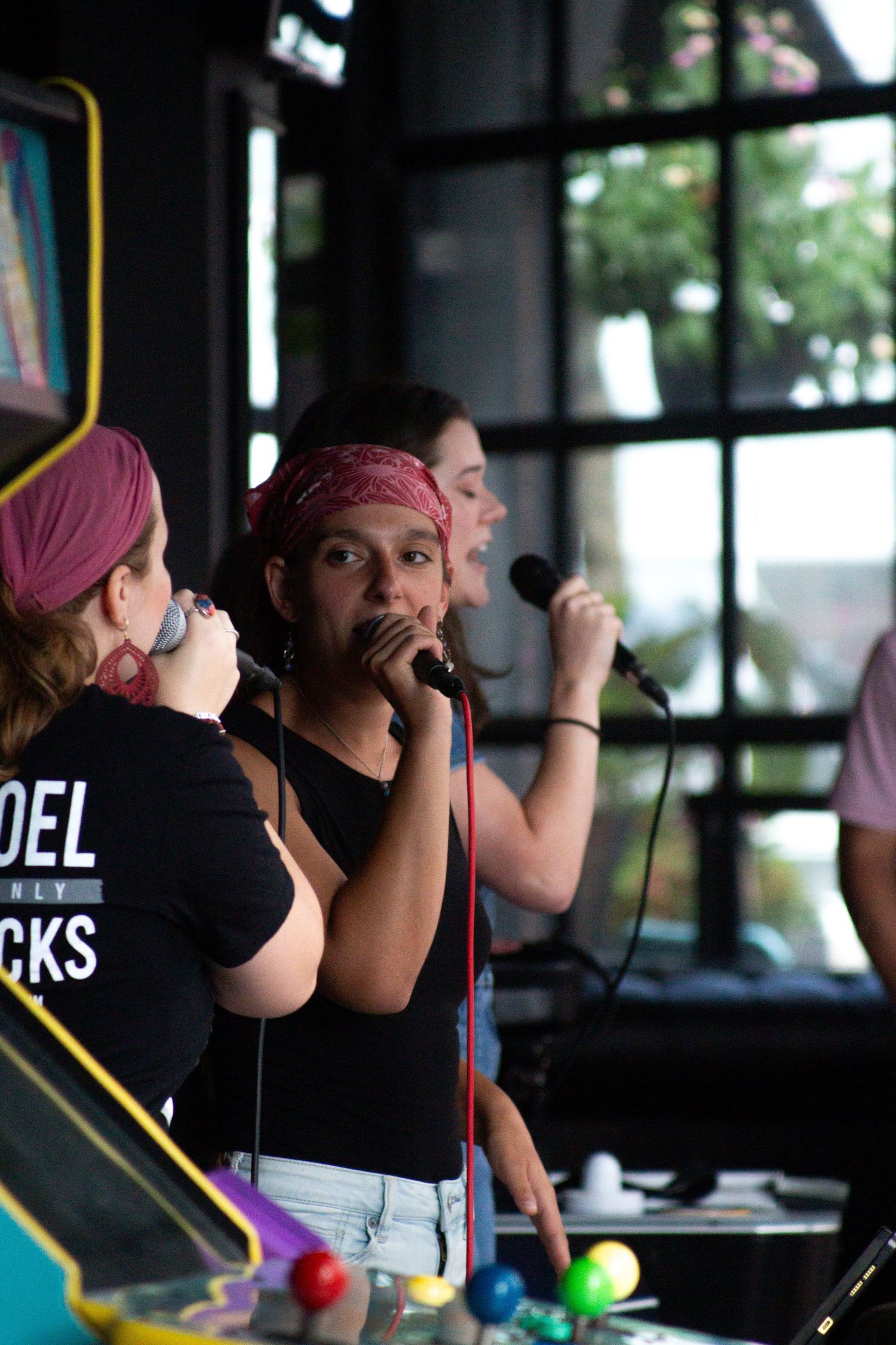 Three women singing into microphones perform together on stage at an indoor music venue.