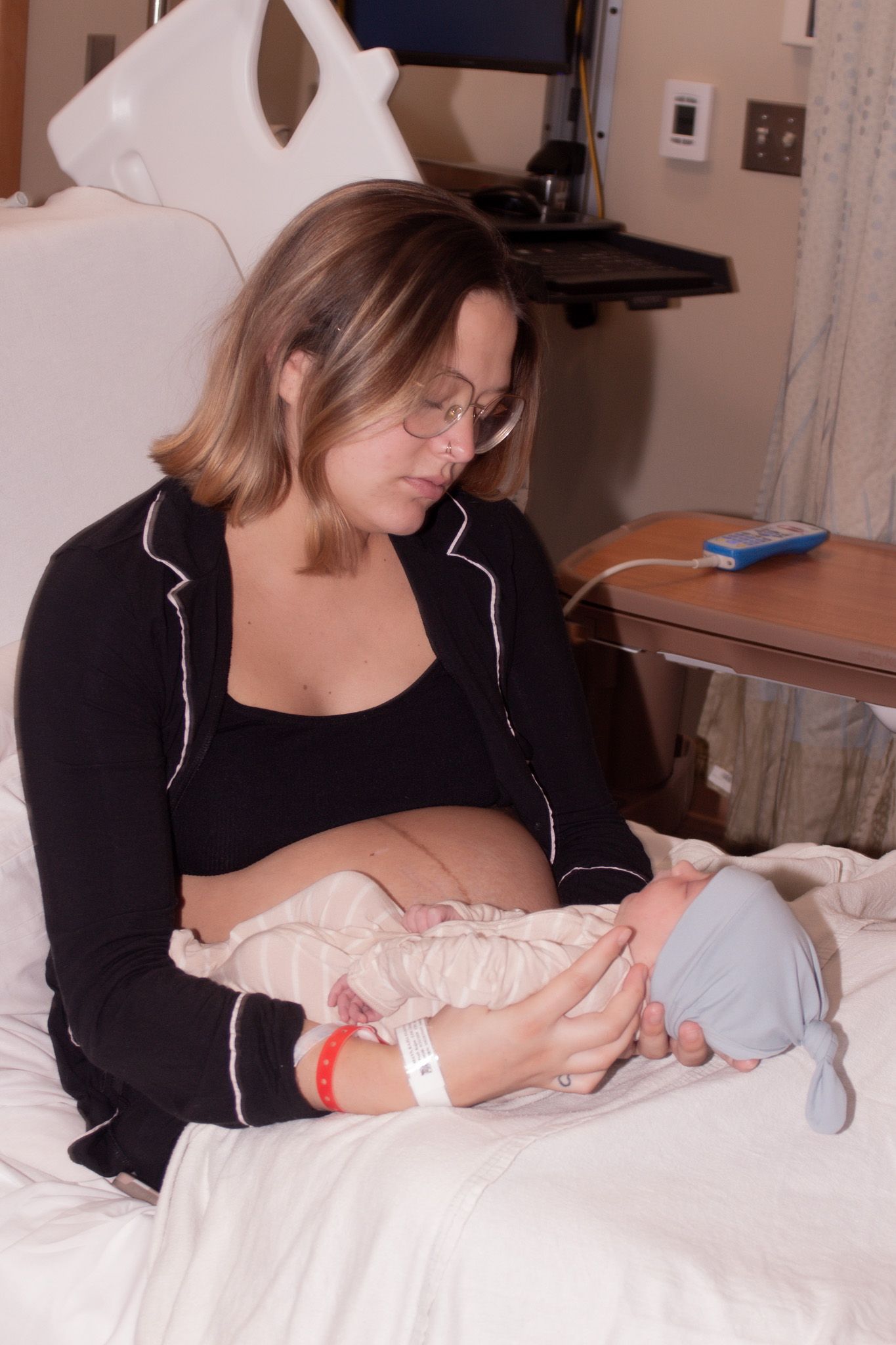 New mother in black pajamas sitting in hospital bed cradling her newborn baby.