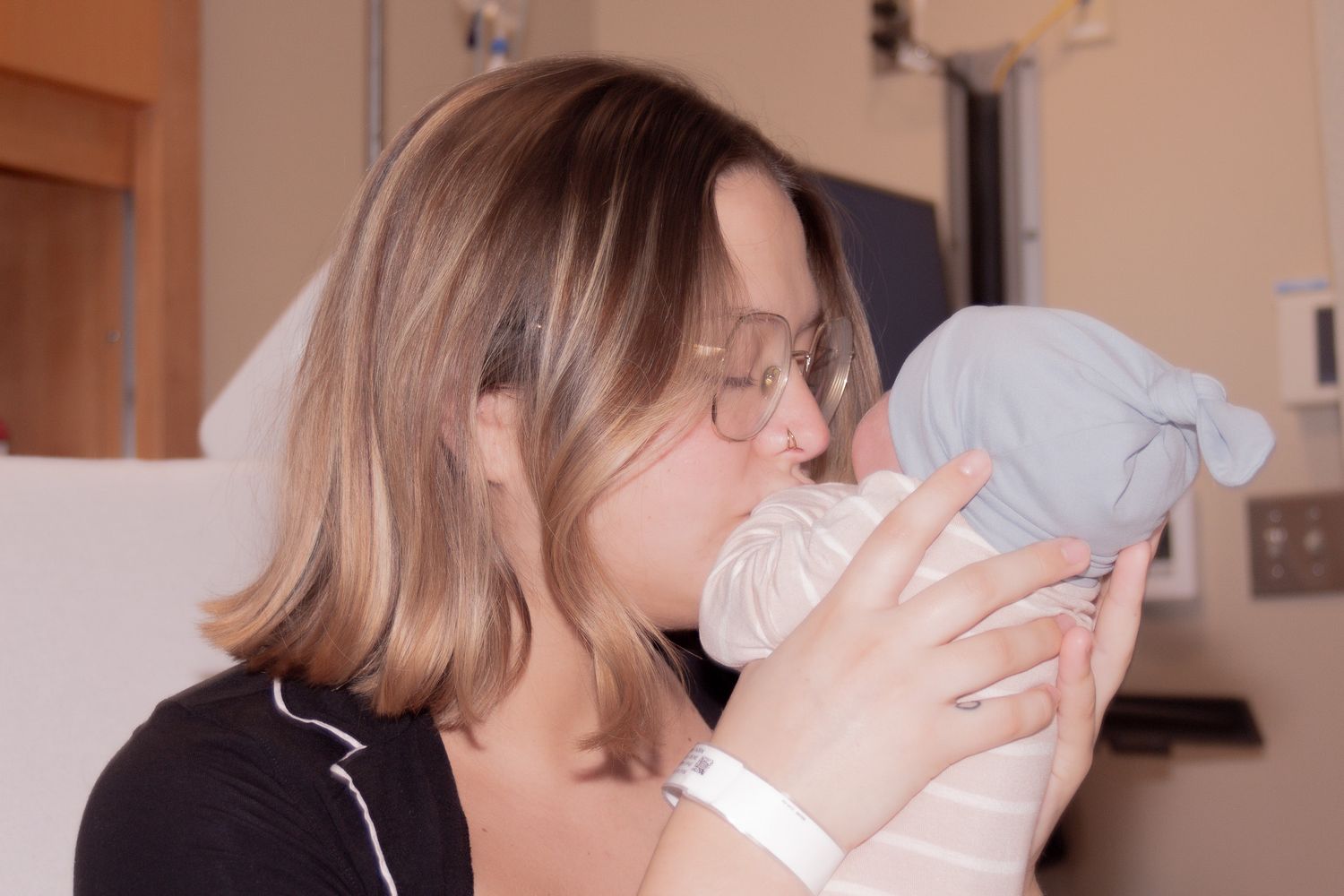 Mother with glasses kissing her newborn baby wrapped in a blue blanket.