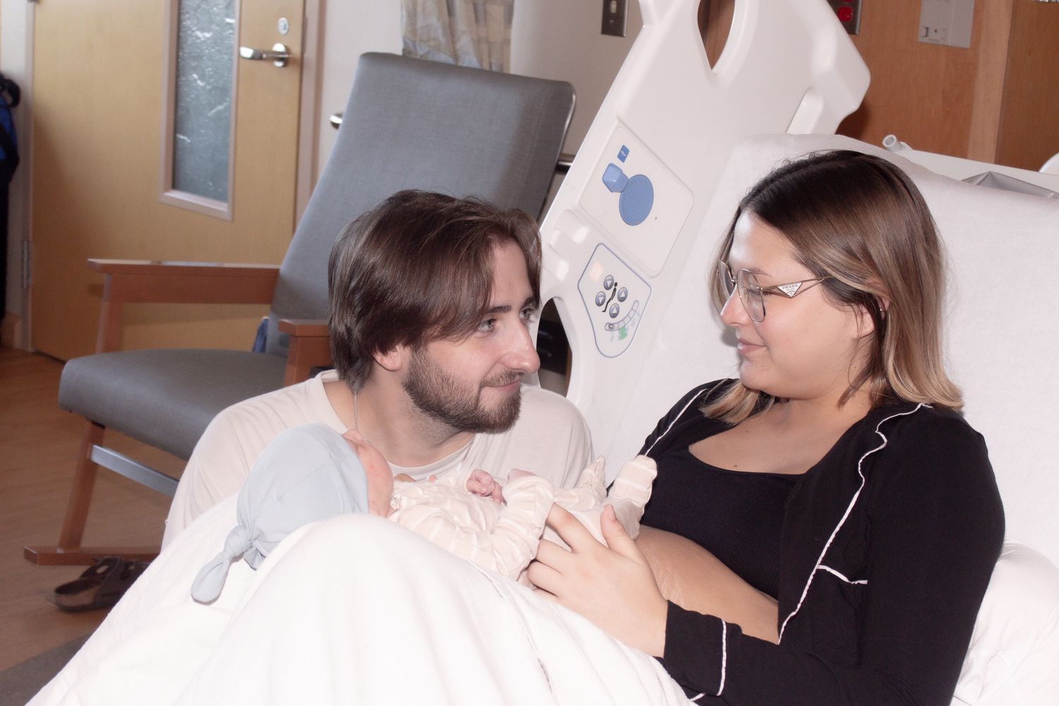 New parents in hospital room lovingly gazing at their newborn baby together after birth.