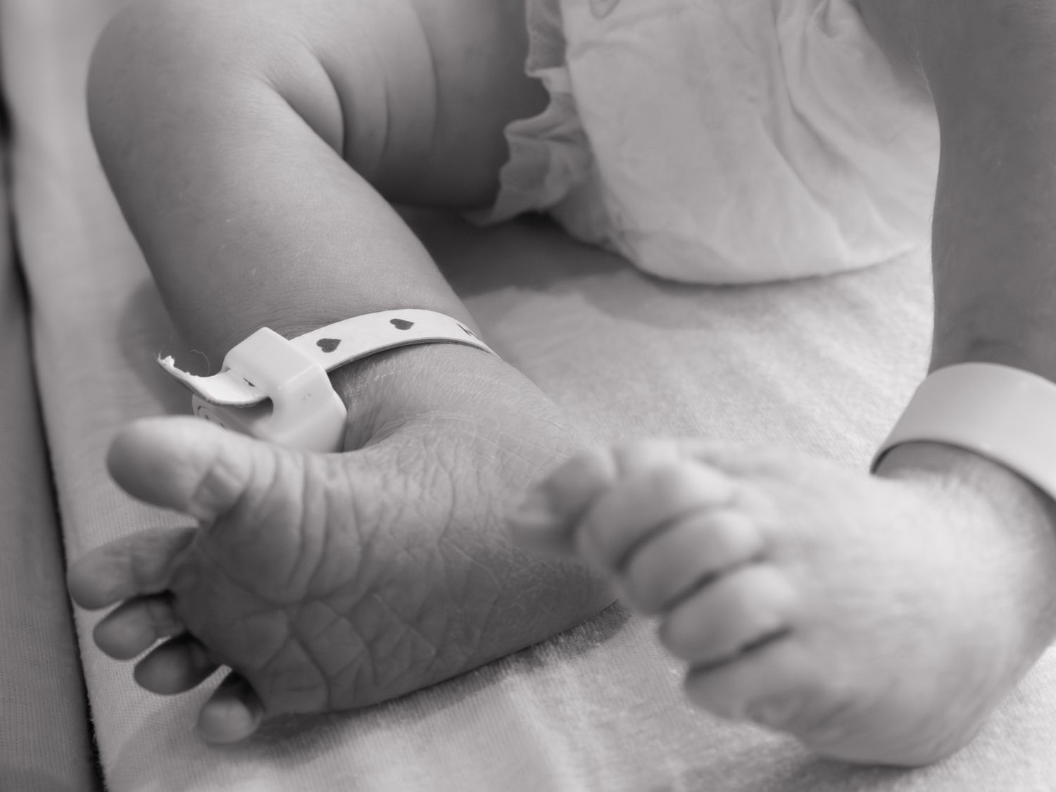 Black and white close-up of newborn baby feet with hospital identification wristband.