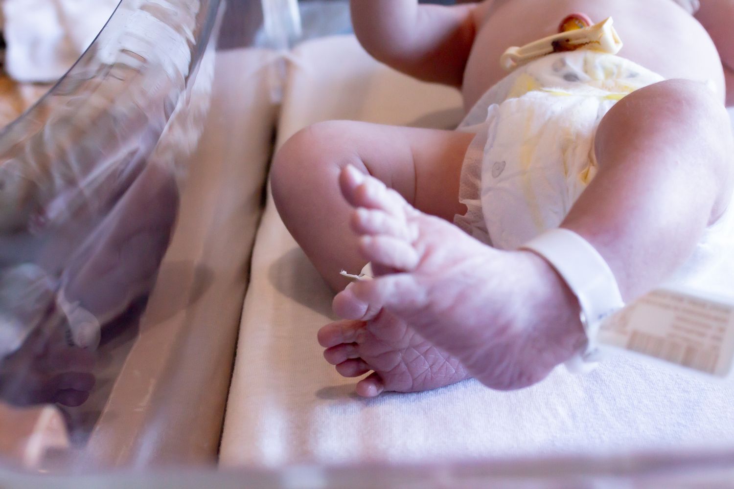 Close-up of newborn baby feet with hospital ID bracelet in a hospital bassinet.