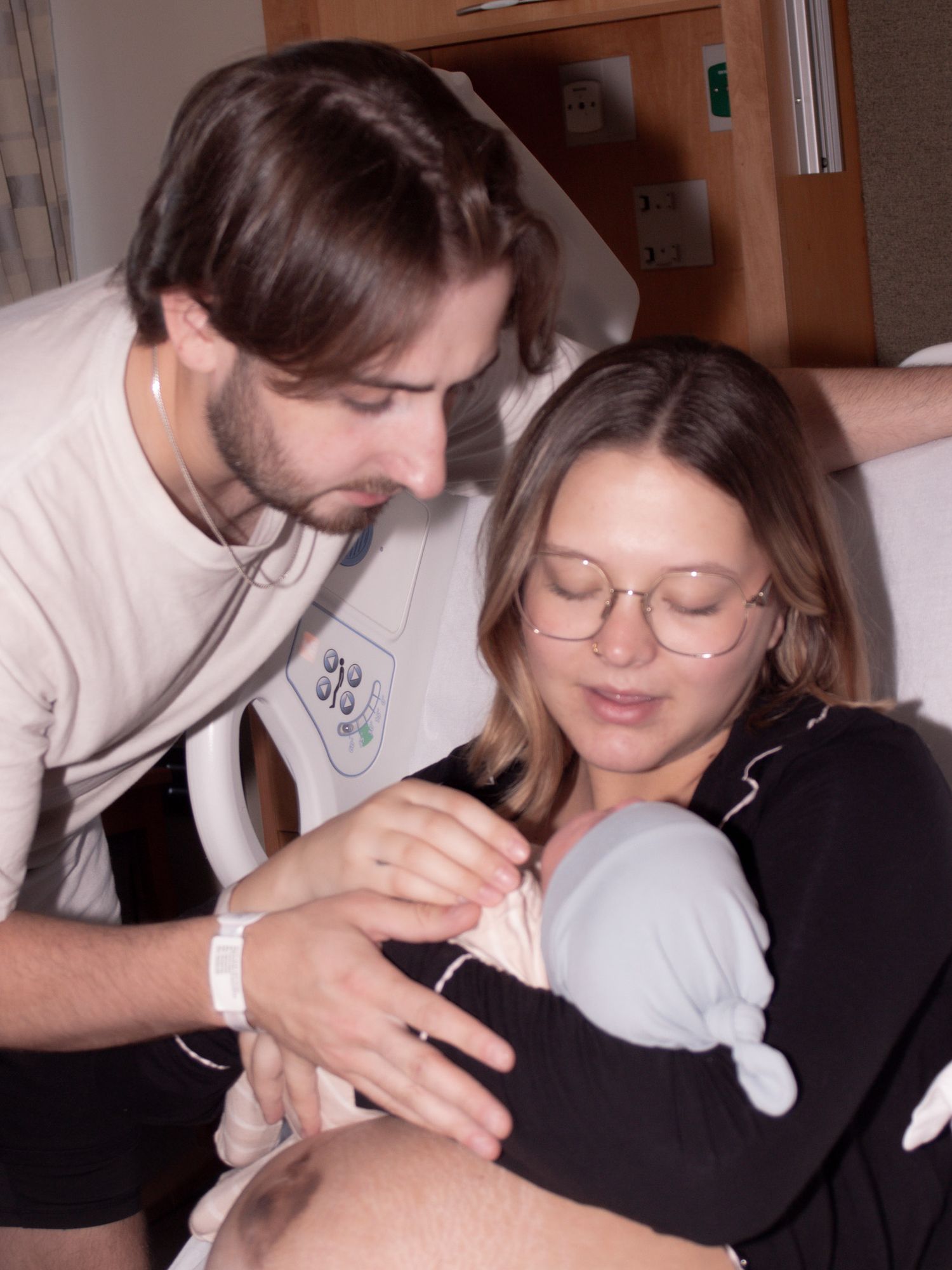 New parents in hospital room bonding together while tenderly holding their newborn baby.
