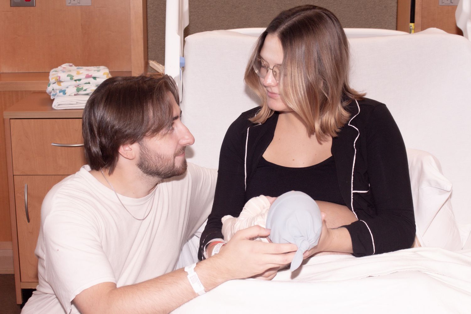 New parents sitting together in hospital room lovingly gazing at their newborn baby.