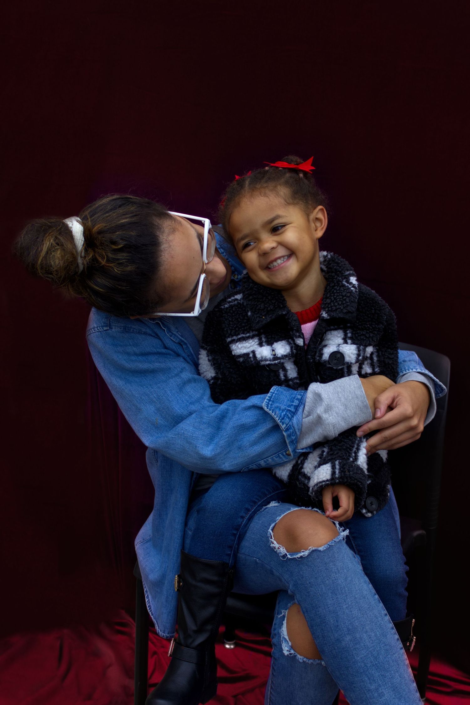 Woman in denim jacket hugging and nuzzling a laughing young girl in a black and white coat.