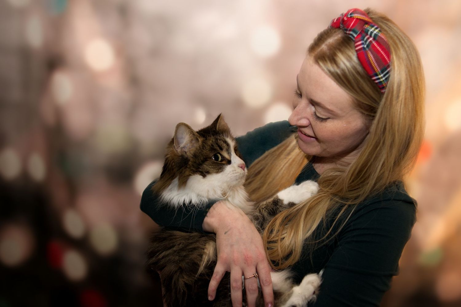 Blonde woman in green top gazes lovingly at a fluffy long-haired cat she is holding.