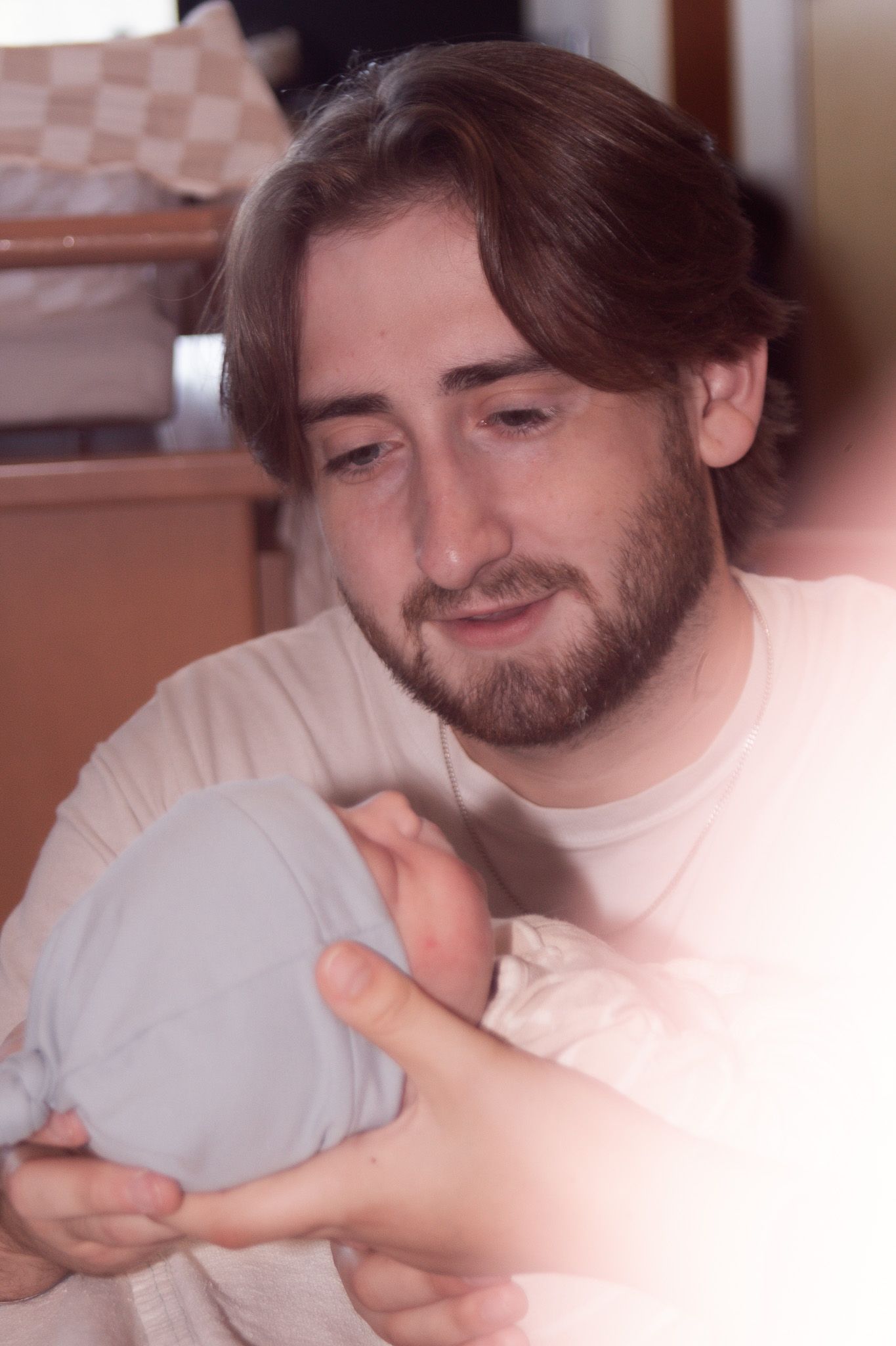 Young bearded man with brown hair emotionally holding a newborn baby.