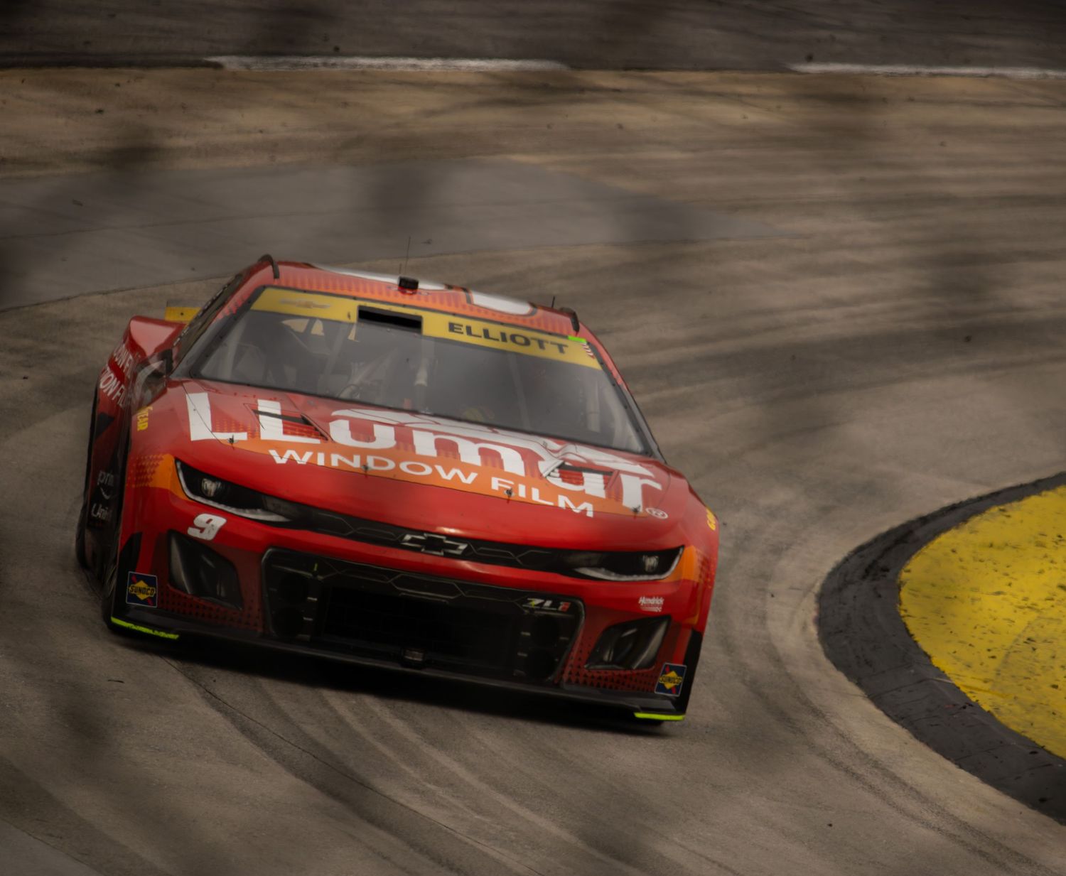 Race cars navigate a turn on the speedway track during a competitive NASCAR event.