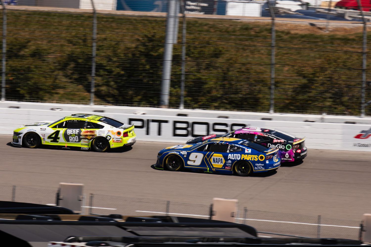 NASCAR race cars compete on an oval track during a professional stock car racing event.