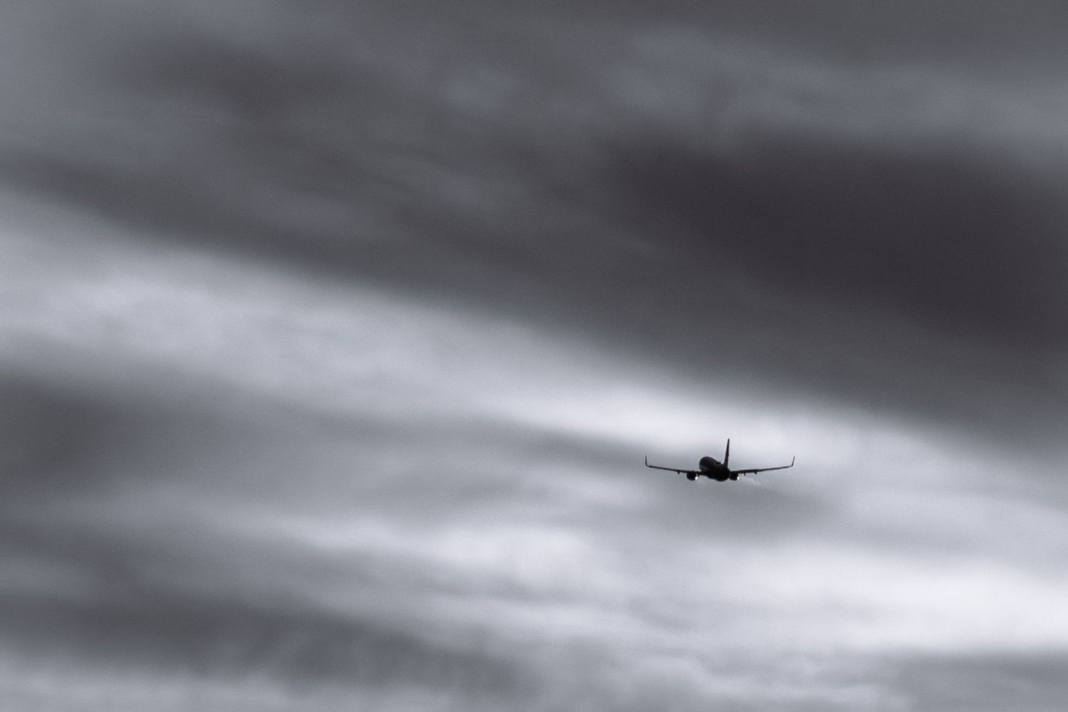 Silhouette of airplane flying through dramatic overcast gray cloudy sky.