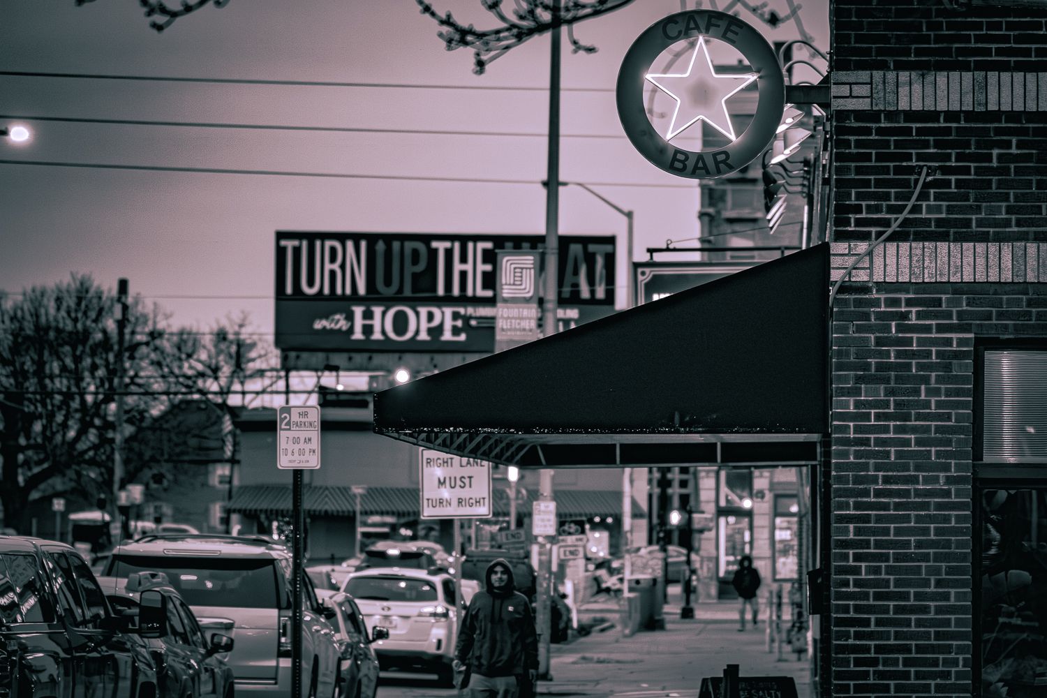 A black and white urban street scene with brick buildings and vintage signage under moody lighting.