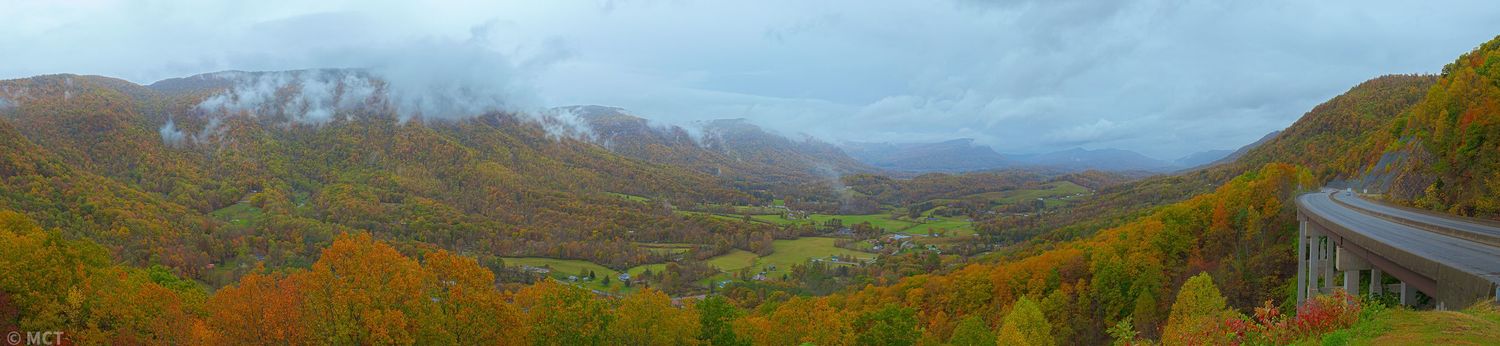 Panoramic mountain landscape view with rolling hills and distant peaks under blue skies.