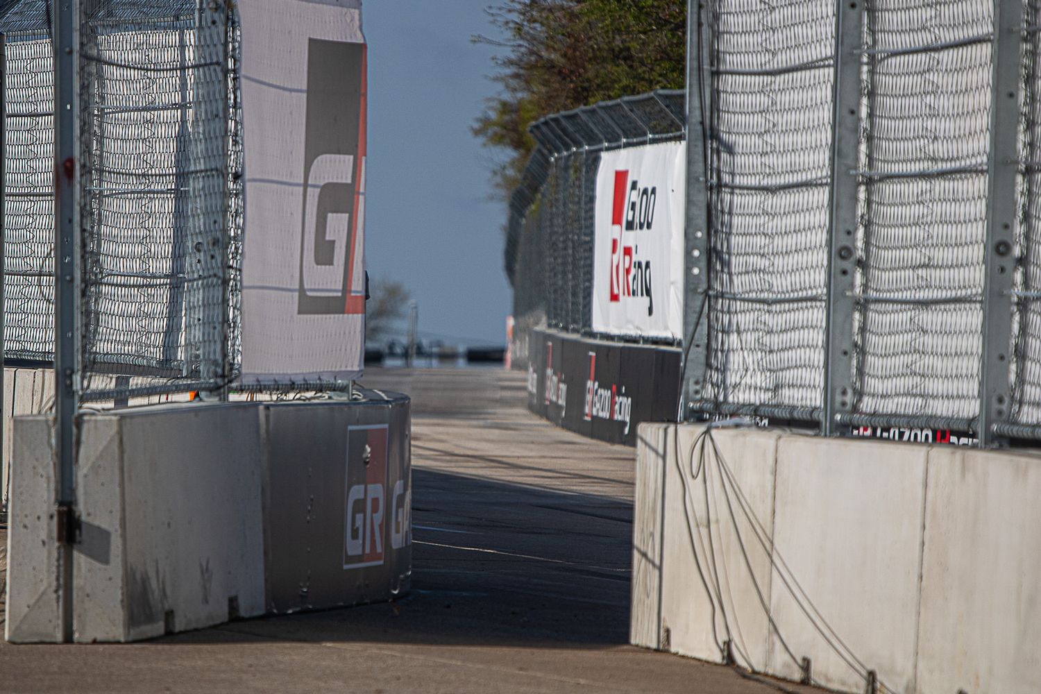 Chain link fence and concrete barriers create a security checkpoint entrance at an outdoor facility.