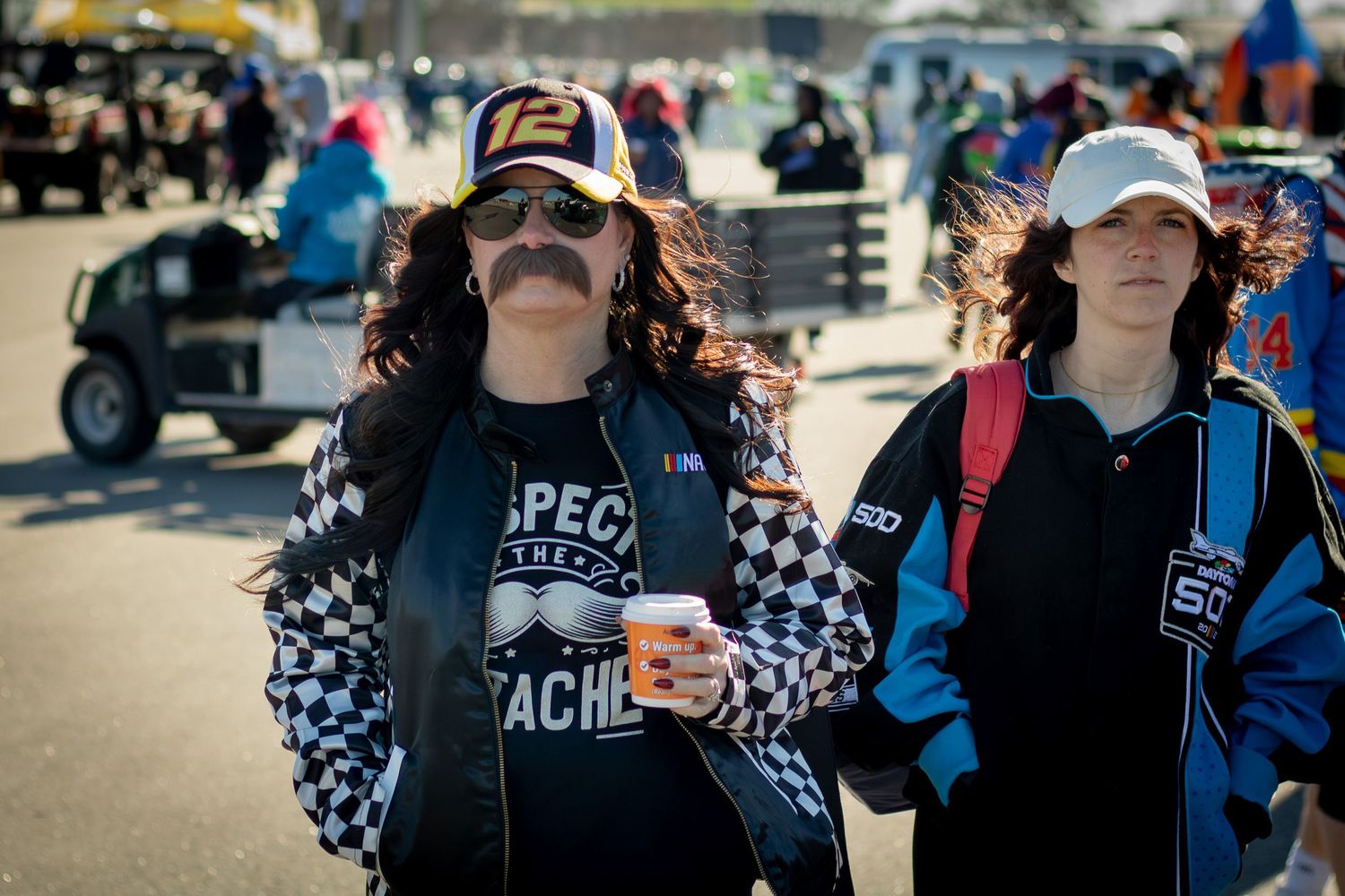 NASCAR fans in racing apparel and hats socialize in the stands during a race event.