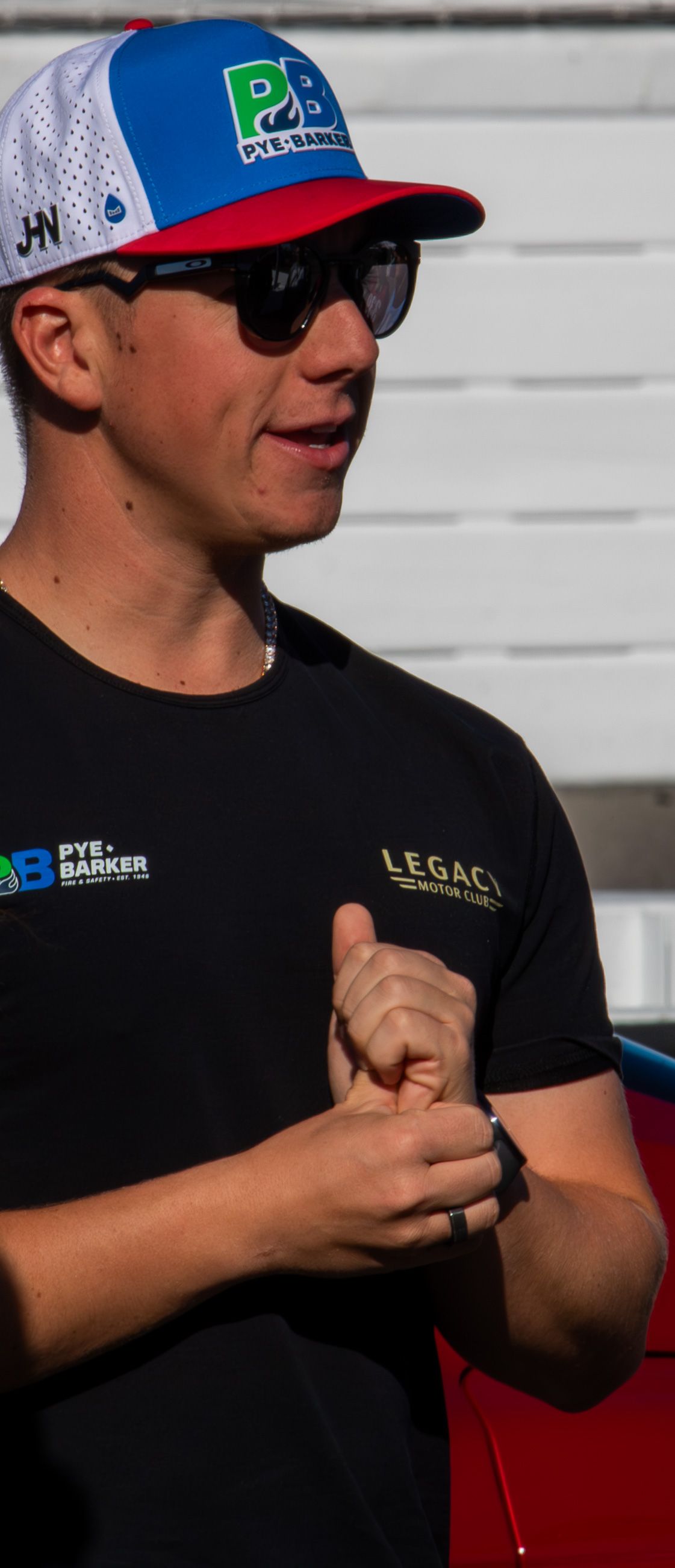 Racing team member wearing a blue and red cap with sunglasses and Legacy branded shirt.