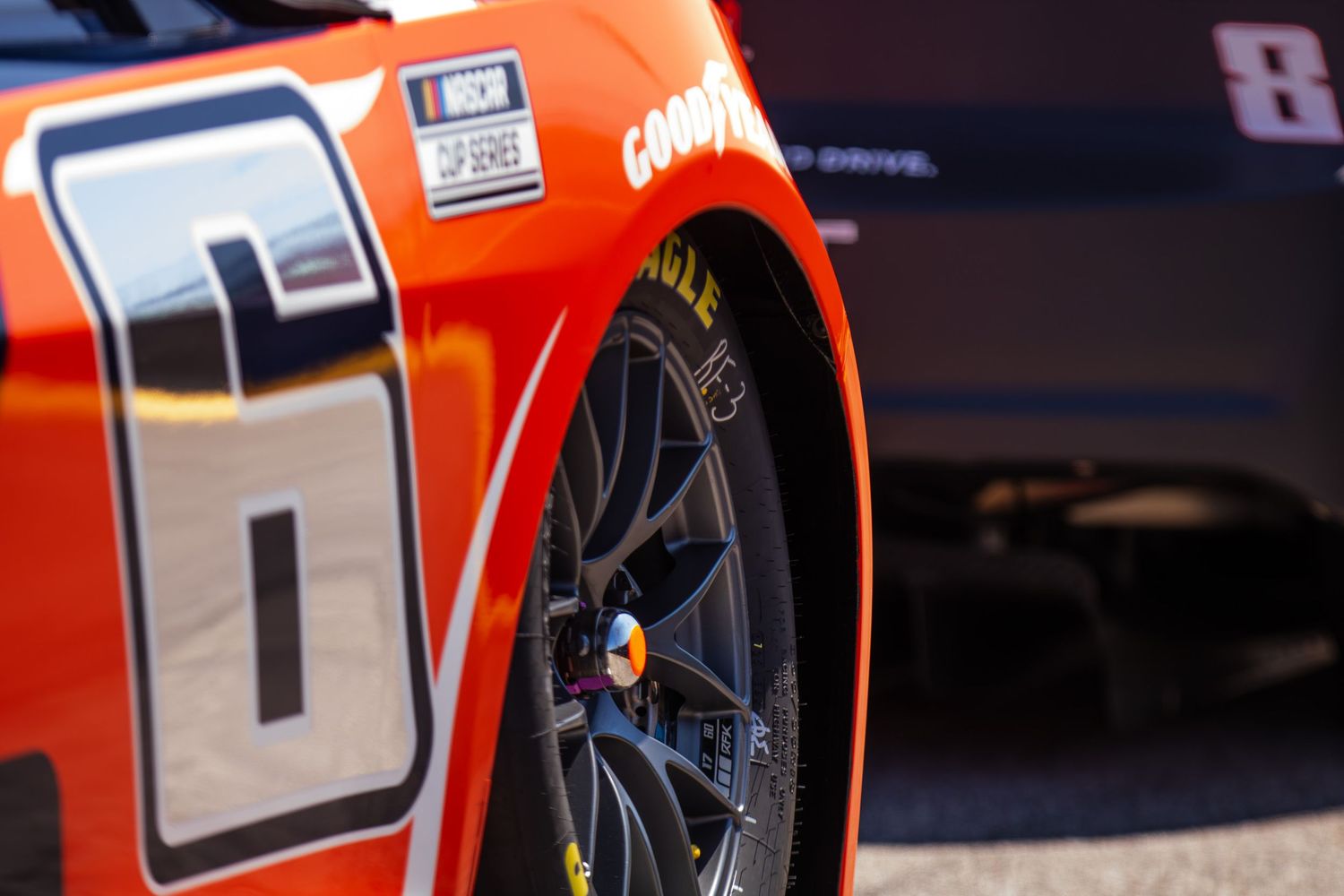 Close-up detail of an orange race car's wheel and side panel with racing numbers.