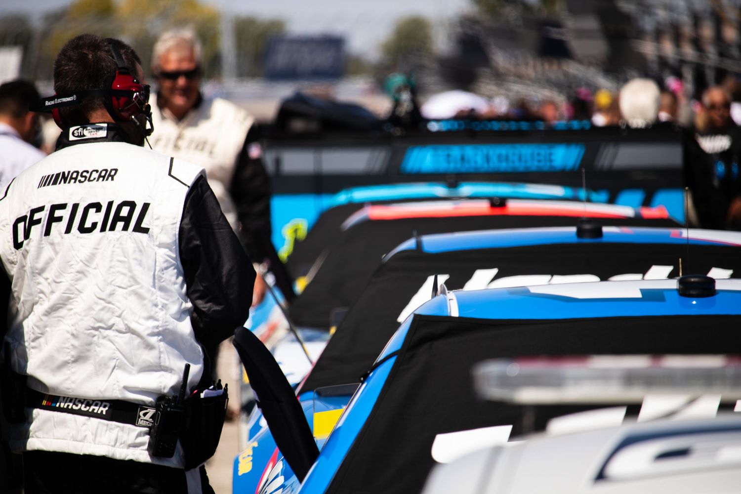 Row of NASCAR race cars with blue and white livery lined up at a racing event.