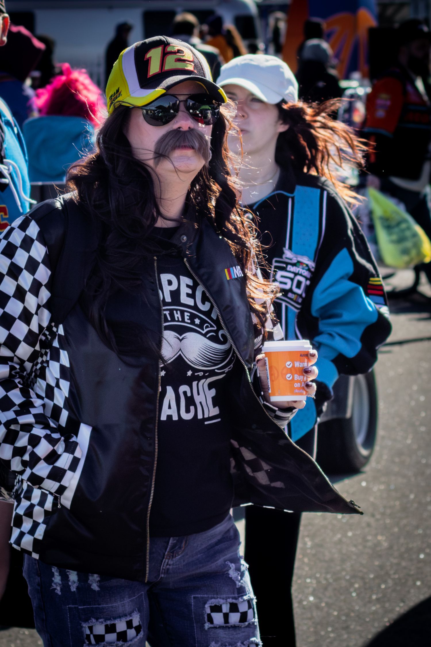 Racing fans wave checkered flags and wear racing merchandise while cheering in the stands.