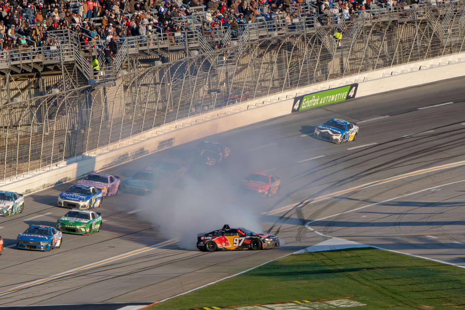 Multiple NASCAR vehicles involved in crash with smoke on speedway during race.
