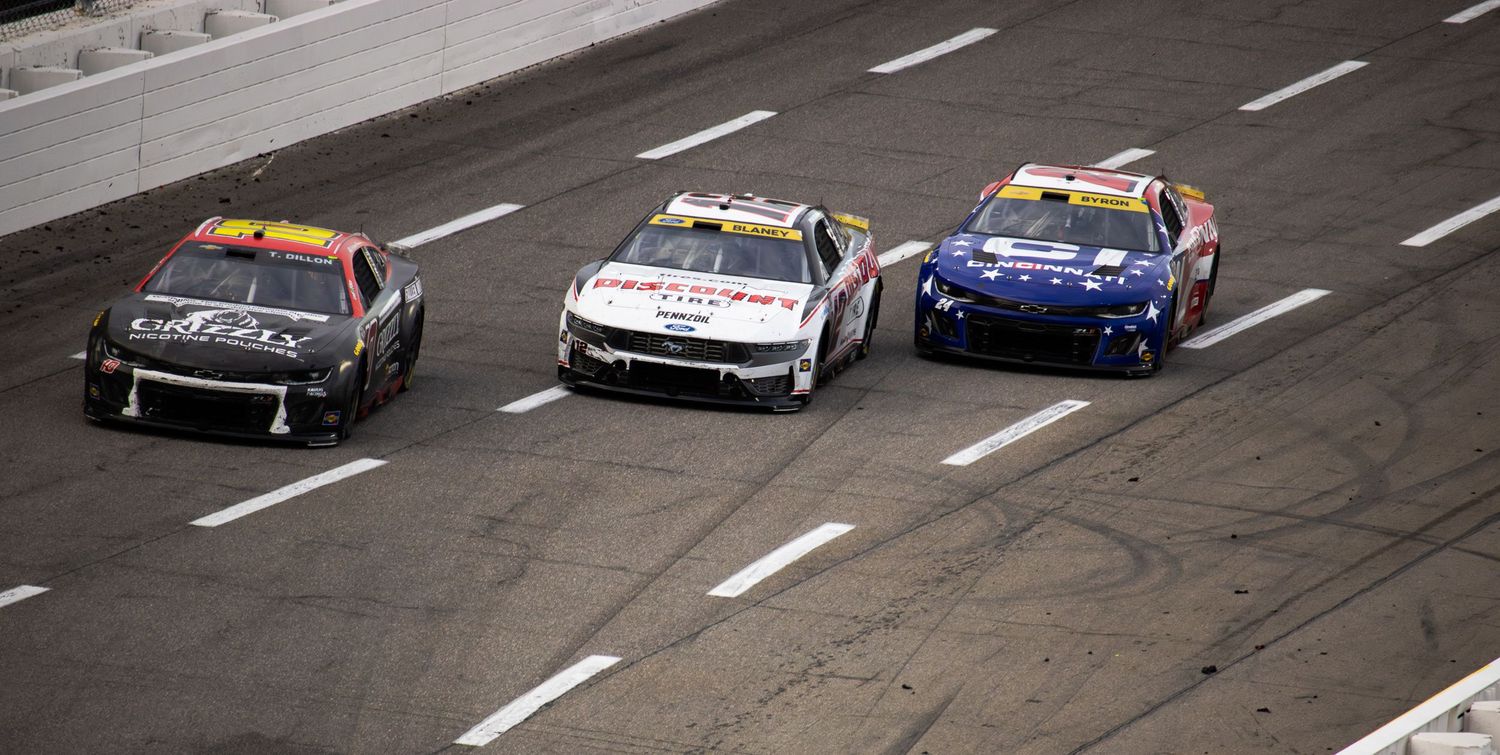 Stock cars line up in formation on the banked racetrack during a NASCAR race.