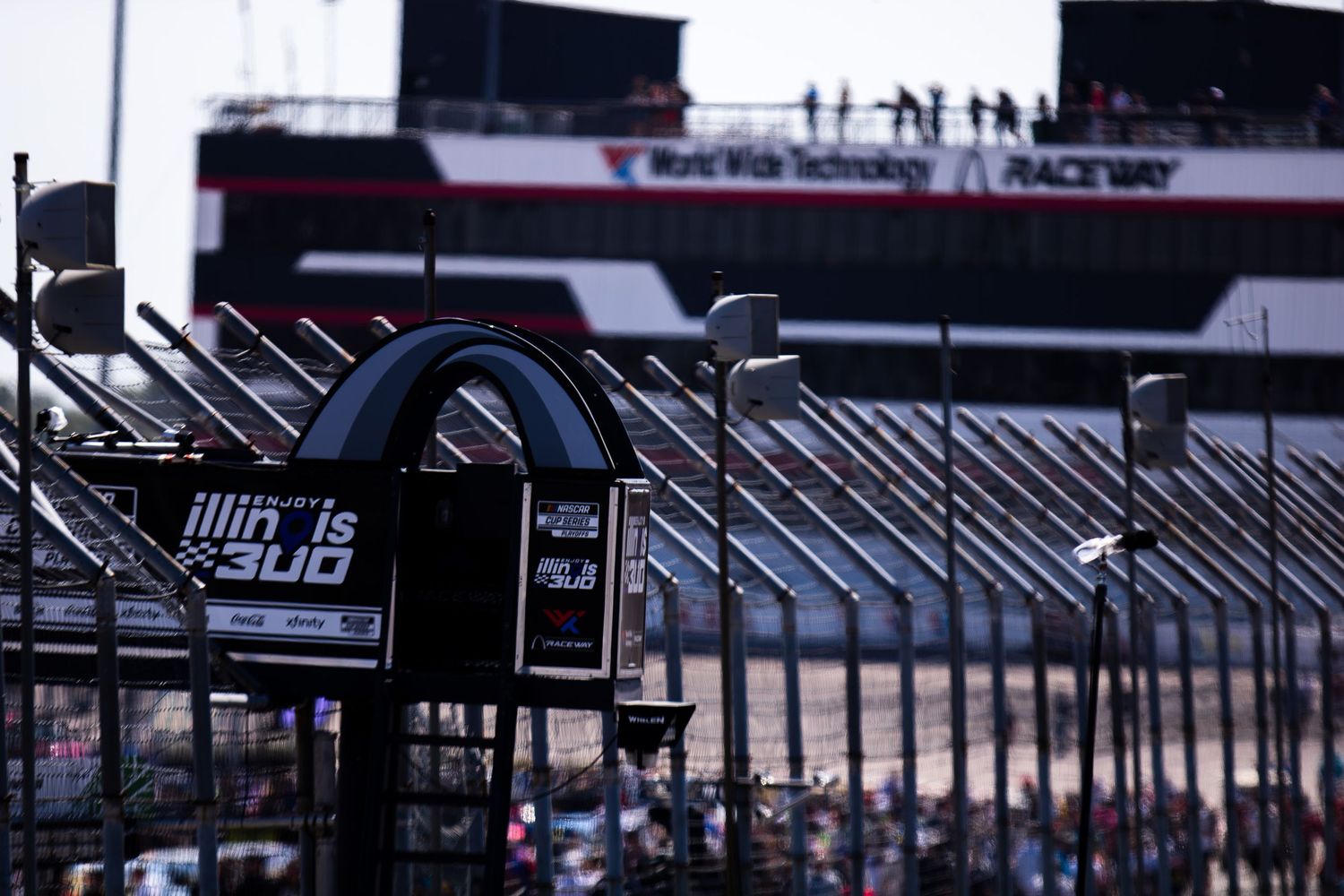 NASCAR race cars lined up at a racing facility with crew members and equipment visible in the background.