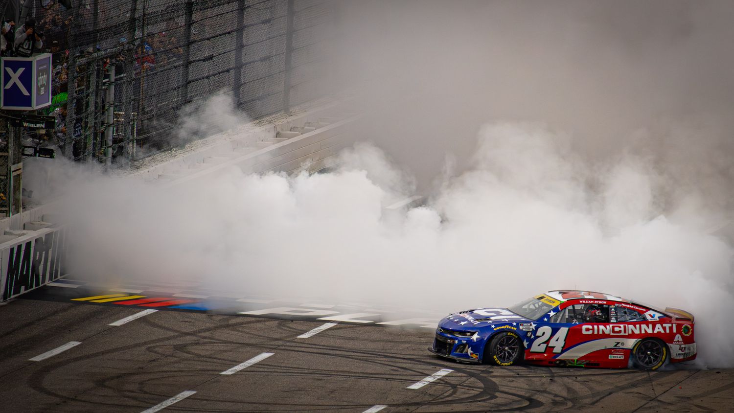 Two race cars create massive smoke clouds during simultaneous victory burnouts.